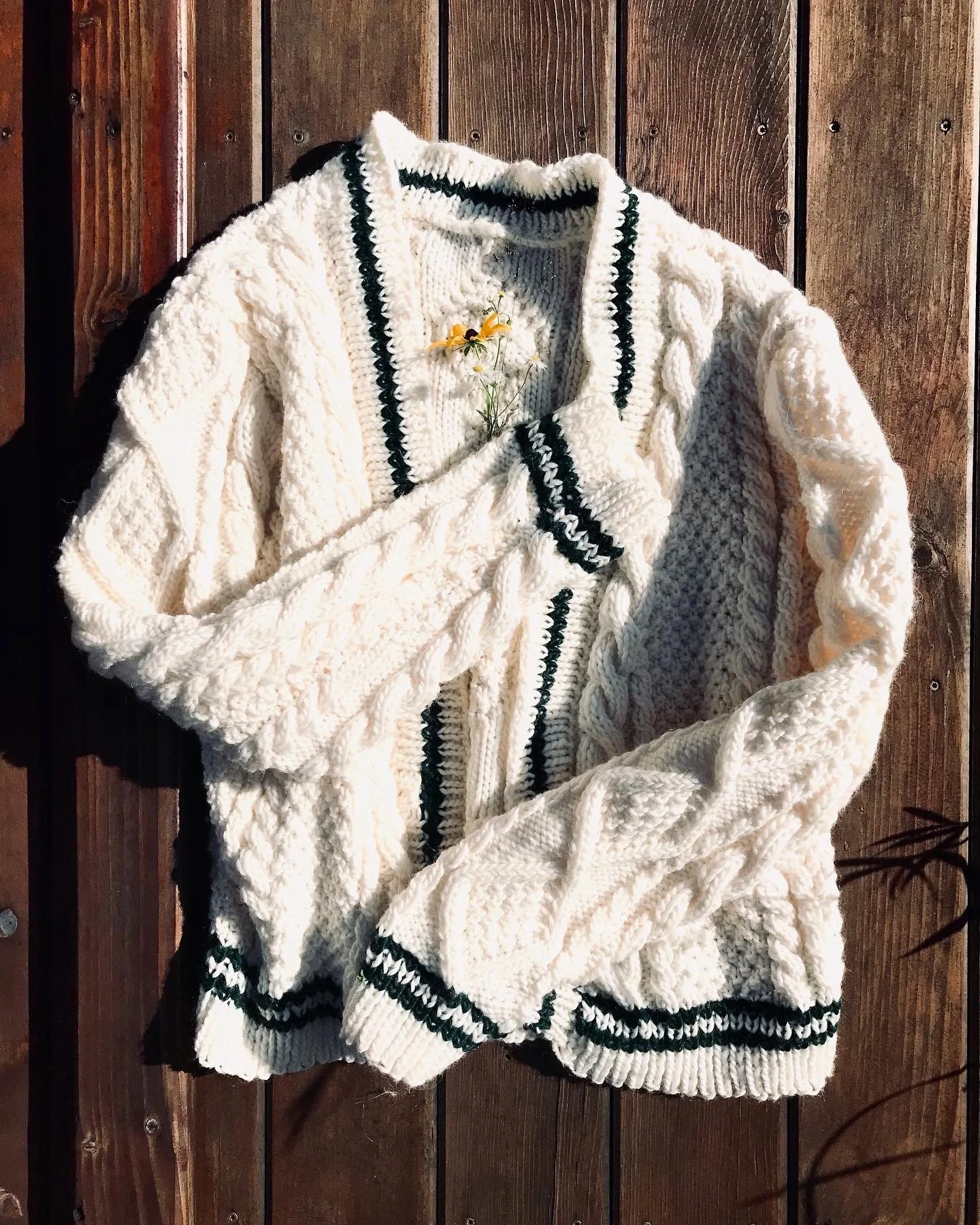 A white cardigan sweater with cable knit details on a wooden background.