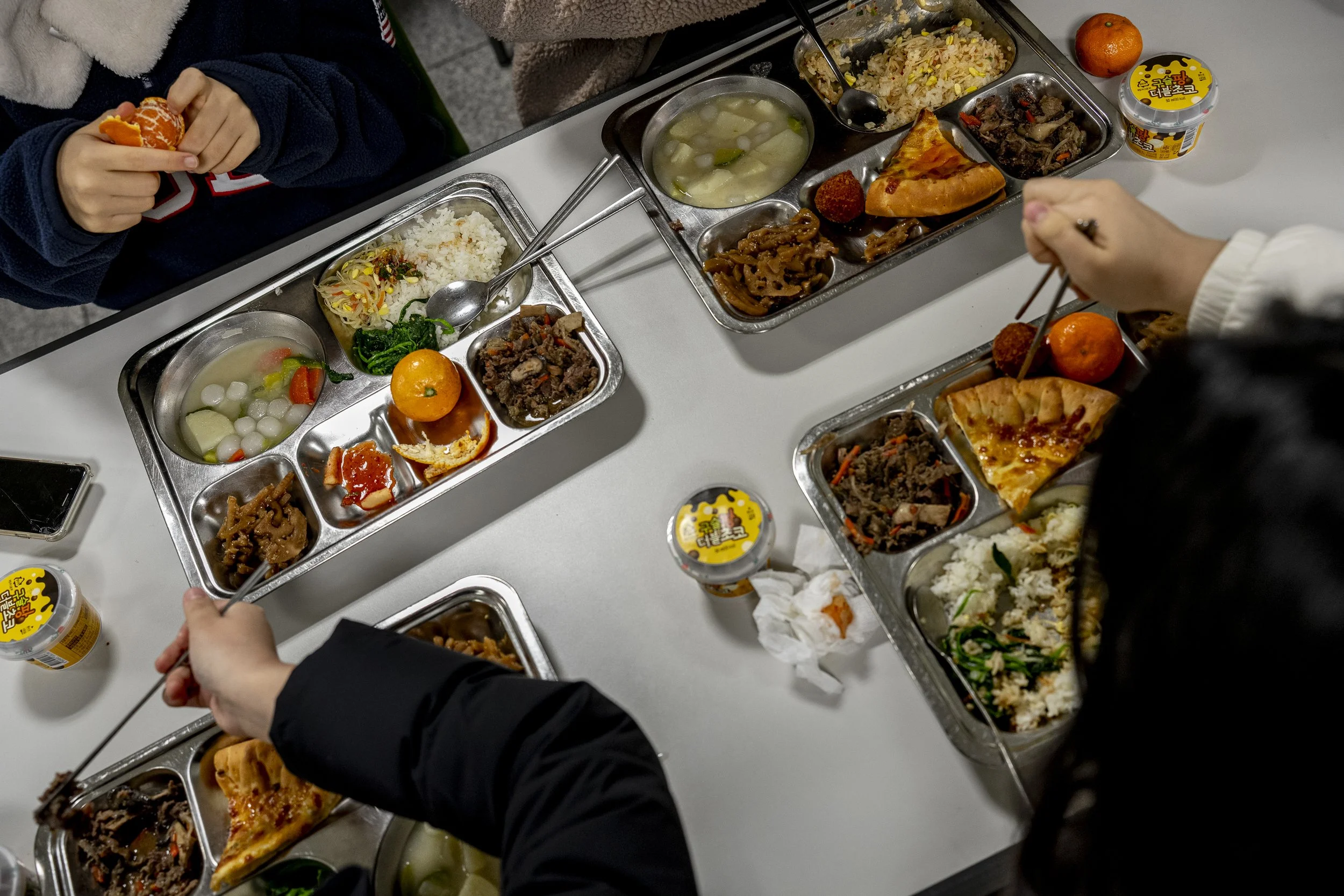 Students and teachers eat lunch together, consisting of Korean beef and bean sprout rice, perilla seed potato soup, braised lotus root, spinach, pizza, radish kimchi, tangerine and ice cream.