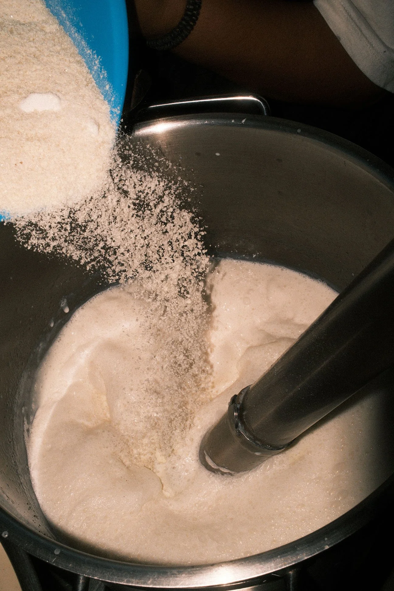 Flour being poured into a blender with liquid to make a batter or dough.