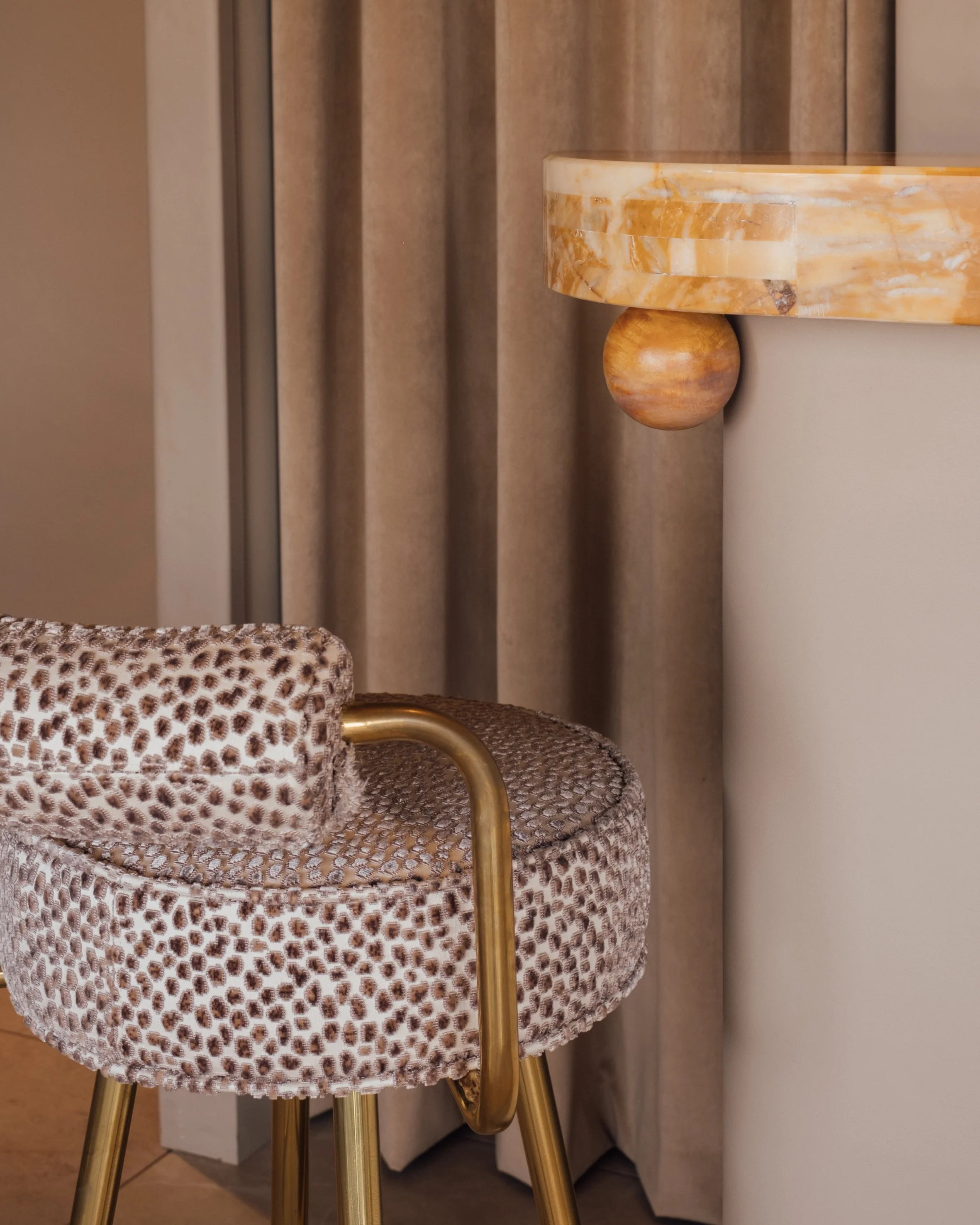 Leopard print upholstered bar stool with gold metallic accents next to a marble-topped counter and floor-length curtains.