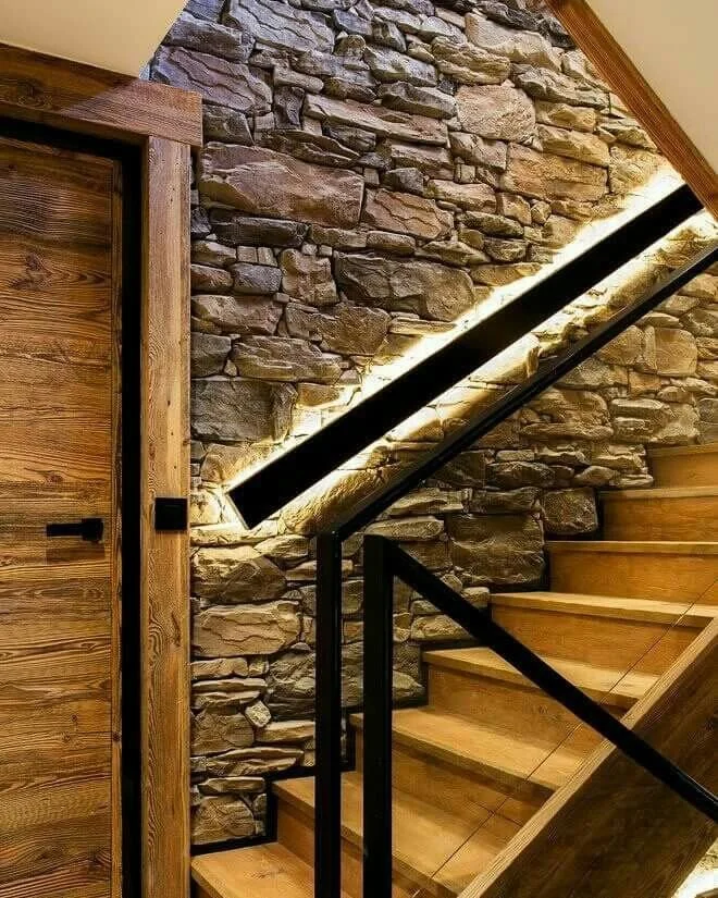 Escalier en bois avec rampe métallique noir, mur en pierre décorative et éclairage LED intégrée.