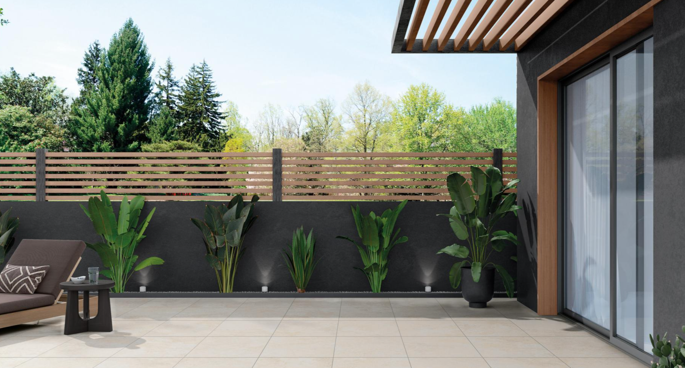Balcon avec plantes vertes, fauteuil, petite table, et vue sur un jardin avec une clôture en bois.