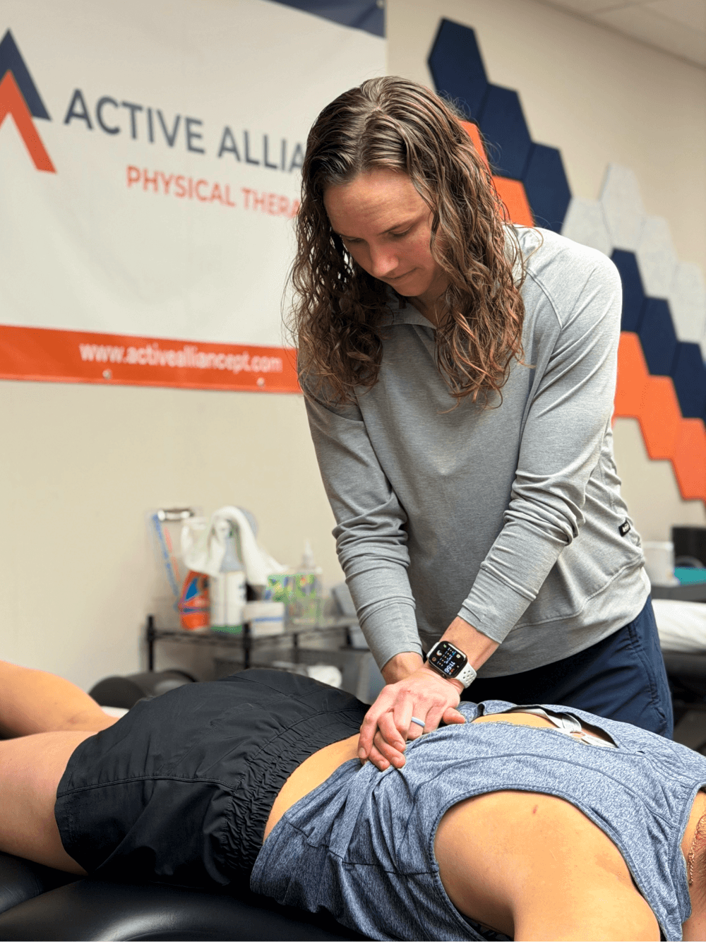 A woman performing a lumbar mobilization on a person lying face down on a table in a wellness or physical therapy setting.