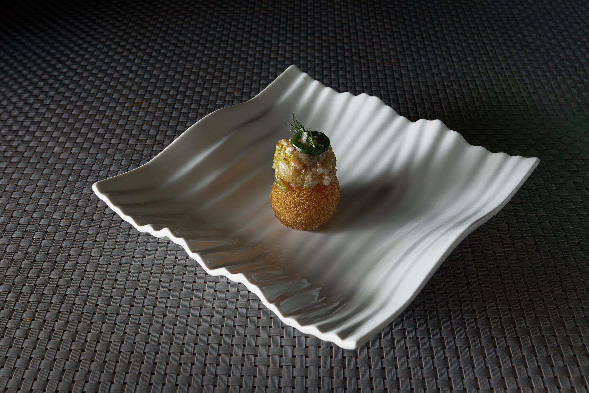 Un aperitivo gourmet presentado en un plato blanco con diseño ondulado.