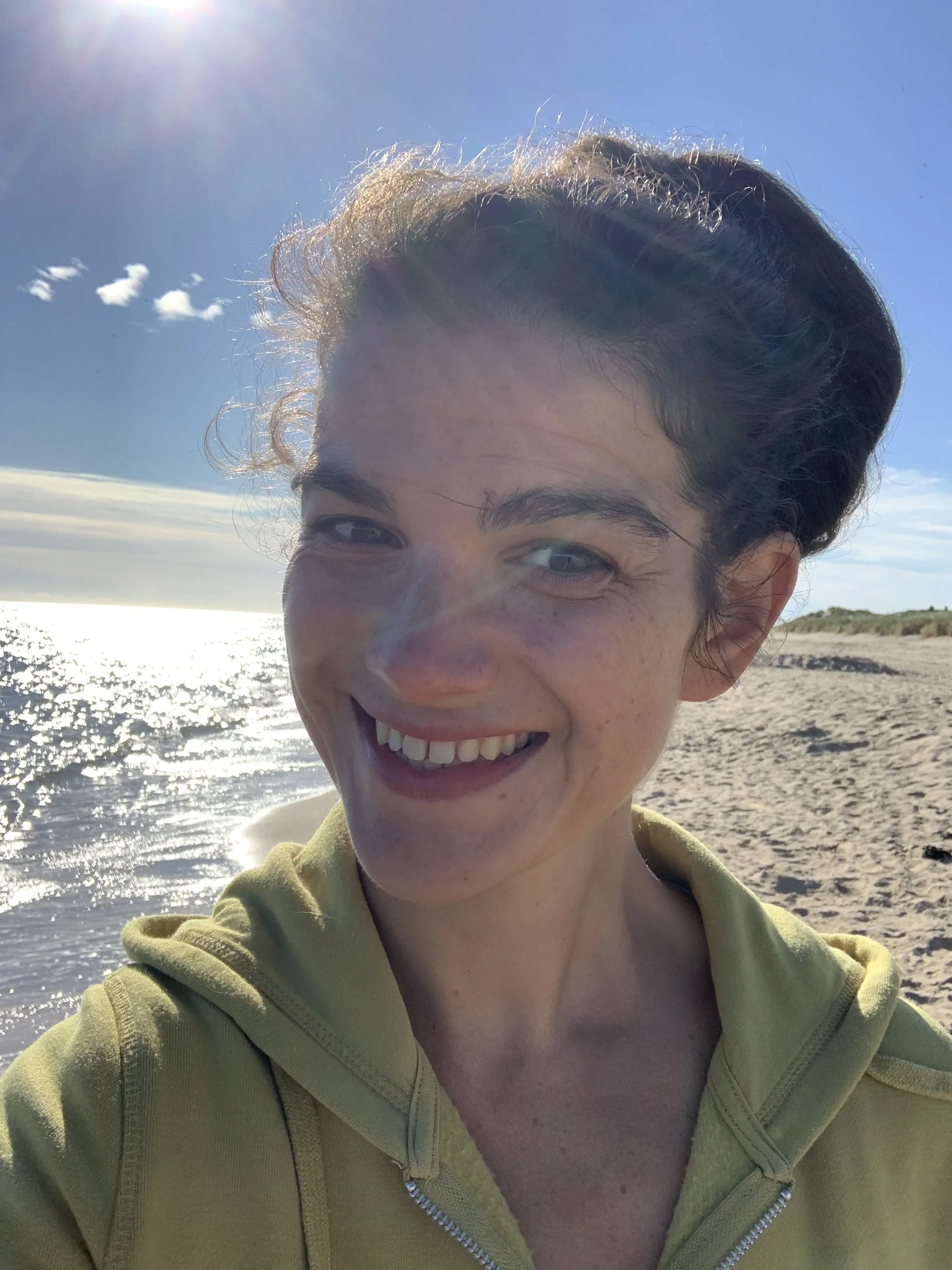 A woman smiling on a sandy beach during daytime with the sun shining in the sky.