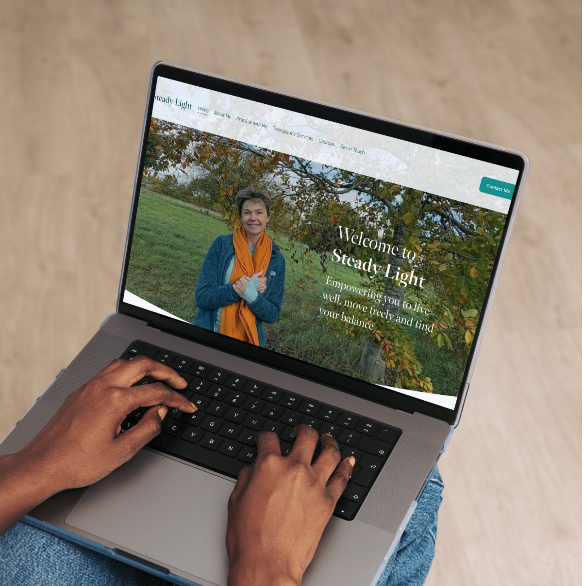 A person using a laptop displaying a website called "Steady Light" with a welcoming woman in a blue jacket and orange scarf standing outdoors in front of a tree with fall foliage. The website promotes living well, moving freely, and finding balance.