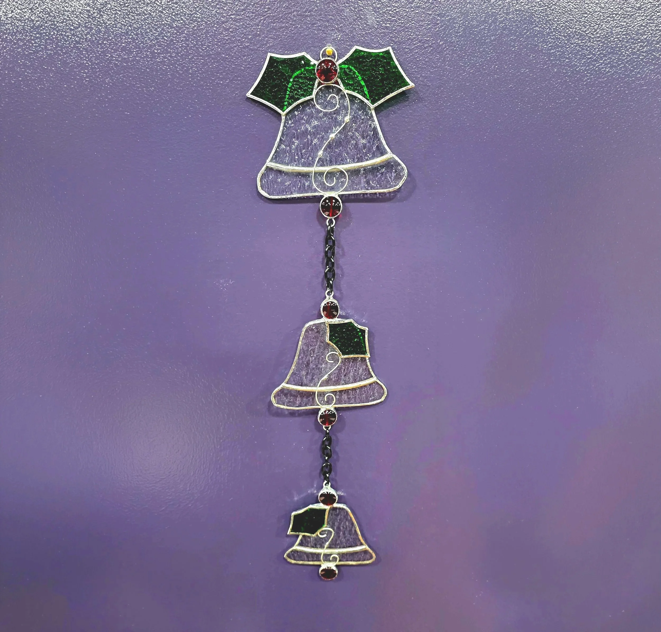 Three stained glass bells assembled in a vertical chain as a hanging decoration for a home.