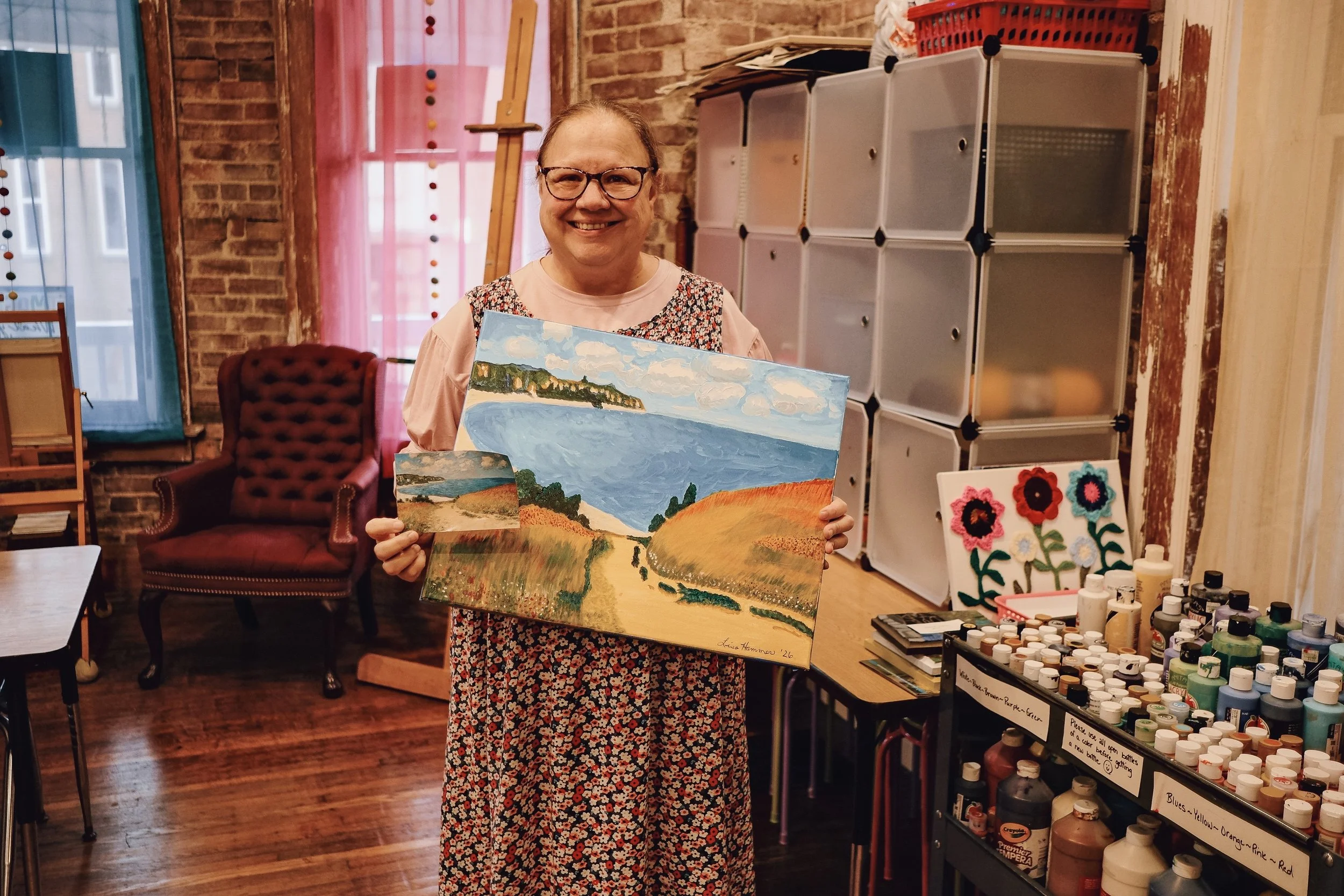Woman displaying her finished acrylic landscape painting.
