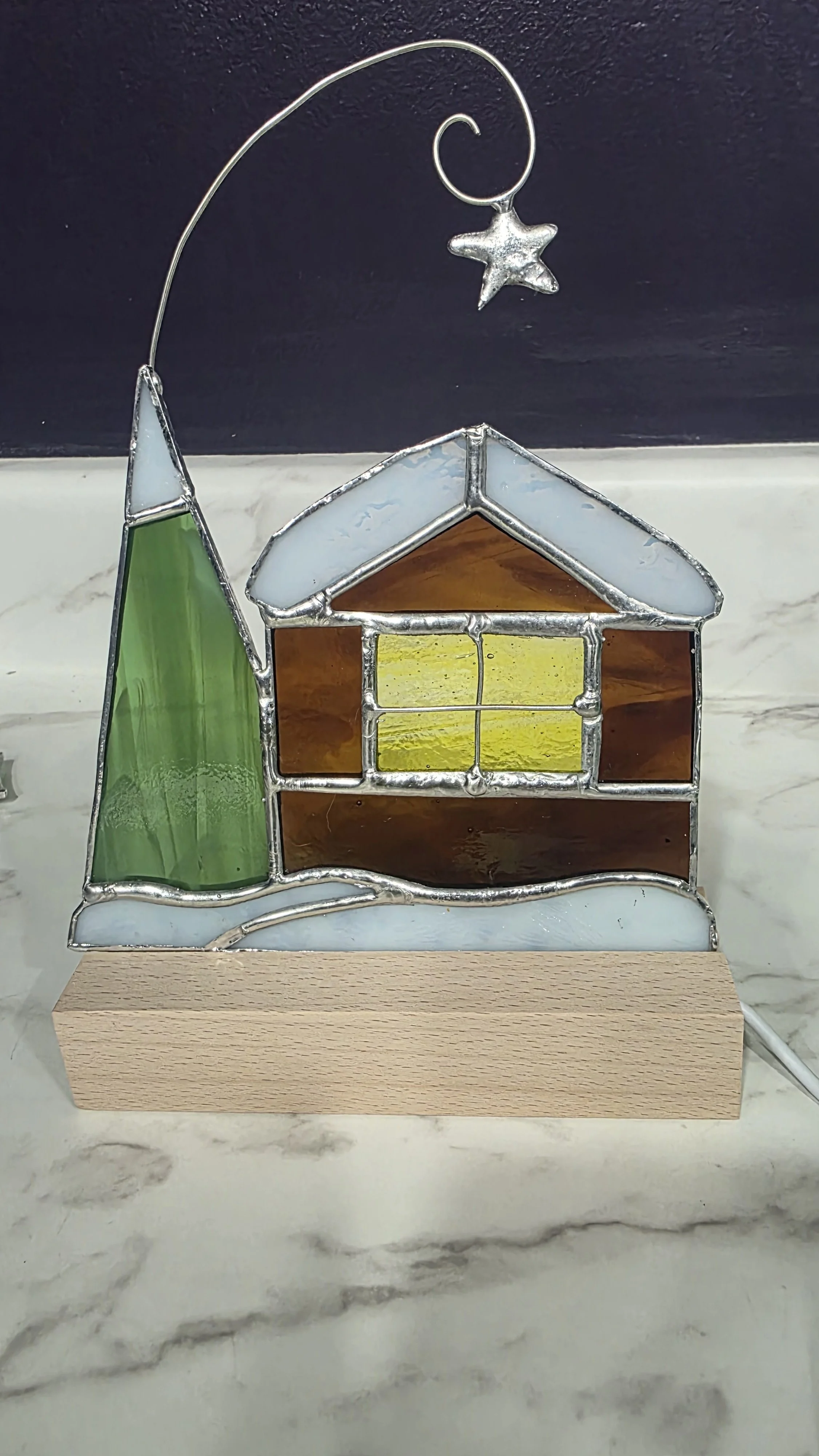 Stained glass snowy cottage including pine tree and building.