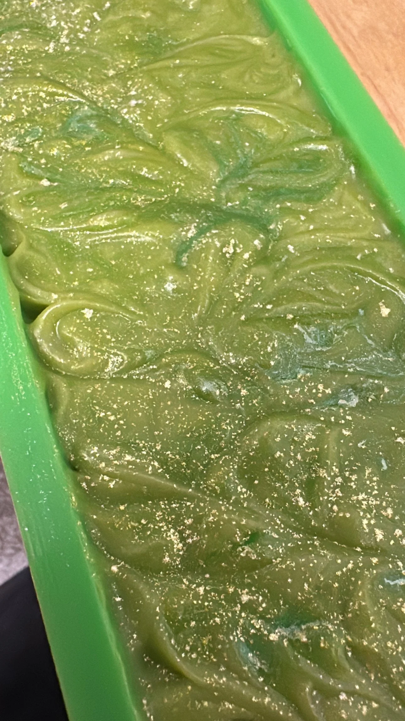 Green colored handmade soap with sparkles setting up in a green soap mold.