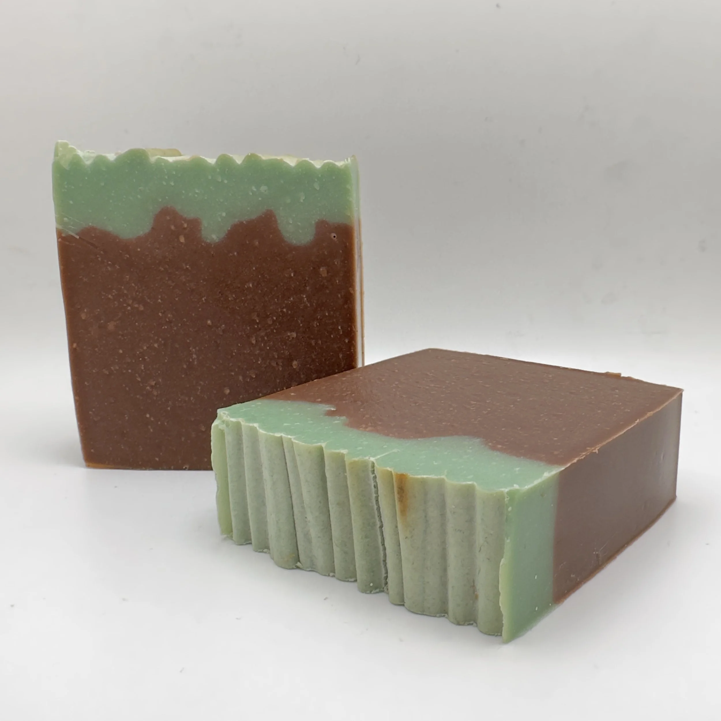 Two handmade soap blocks with green coloring on the top and brown coloring on the bottom.