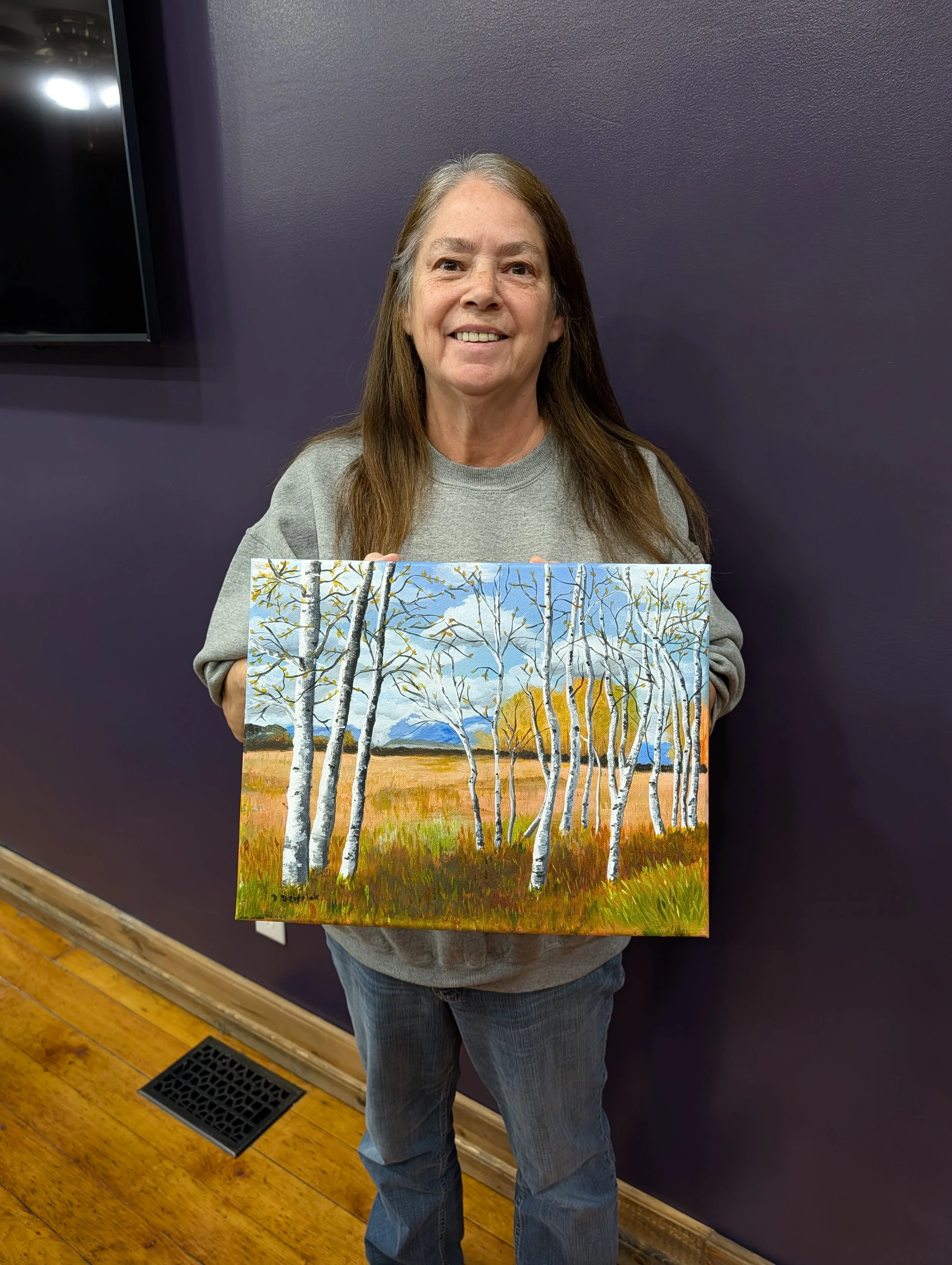 Adult female student displaying her oil painting of birch trees.