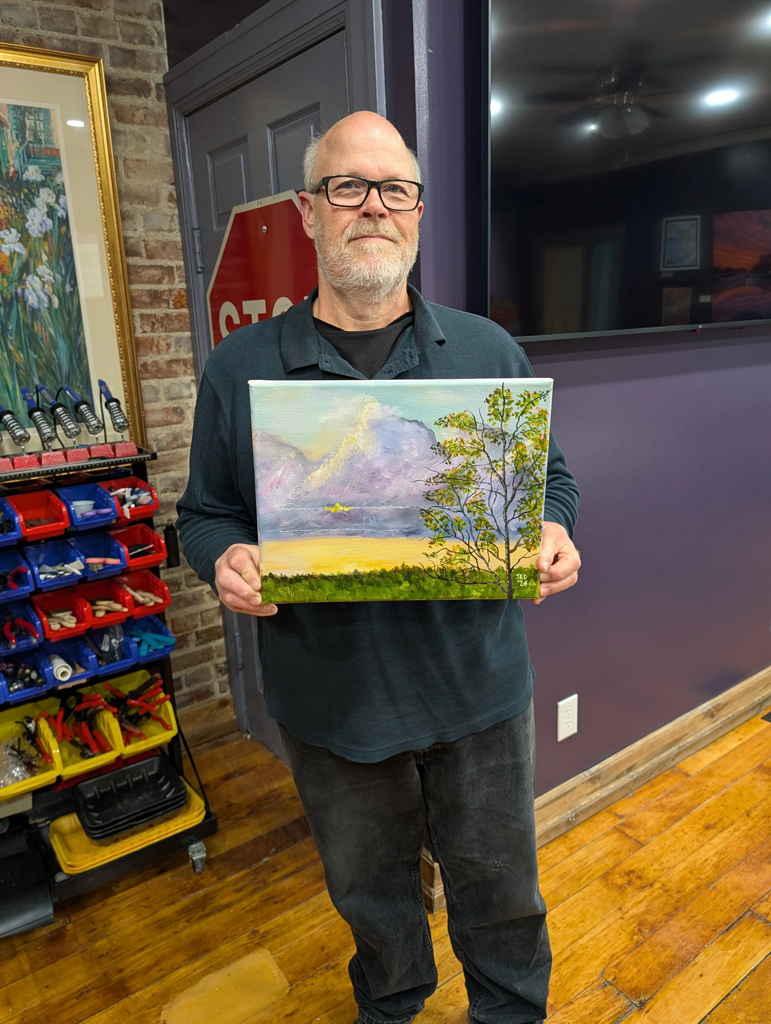 Adult Male student displaying his finished landscape oil painting.