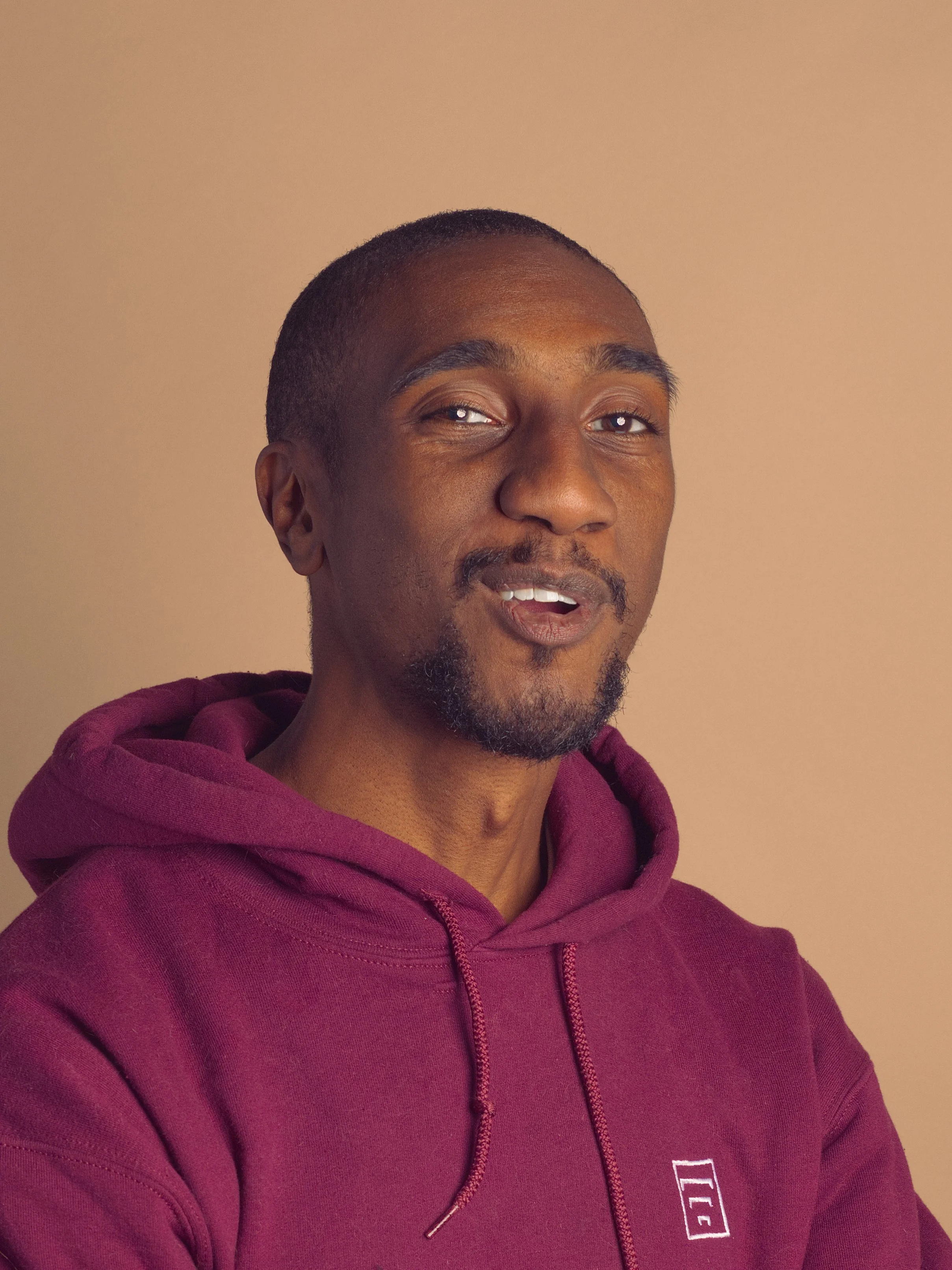 Portrait of photographer Jeffrey Collins wearing a maroon hoodie against a warm studio backdrop.