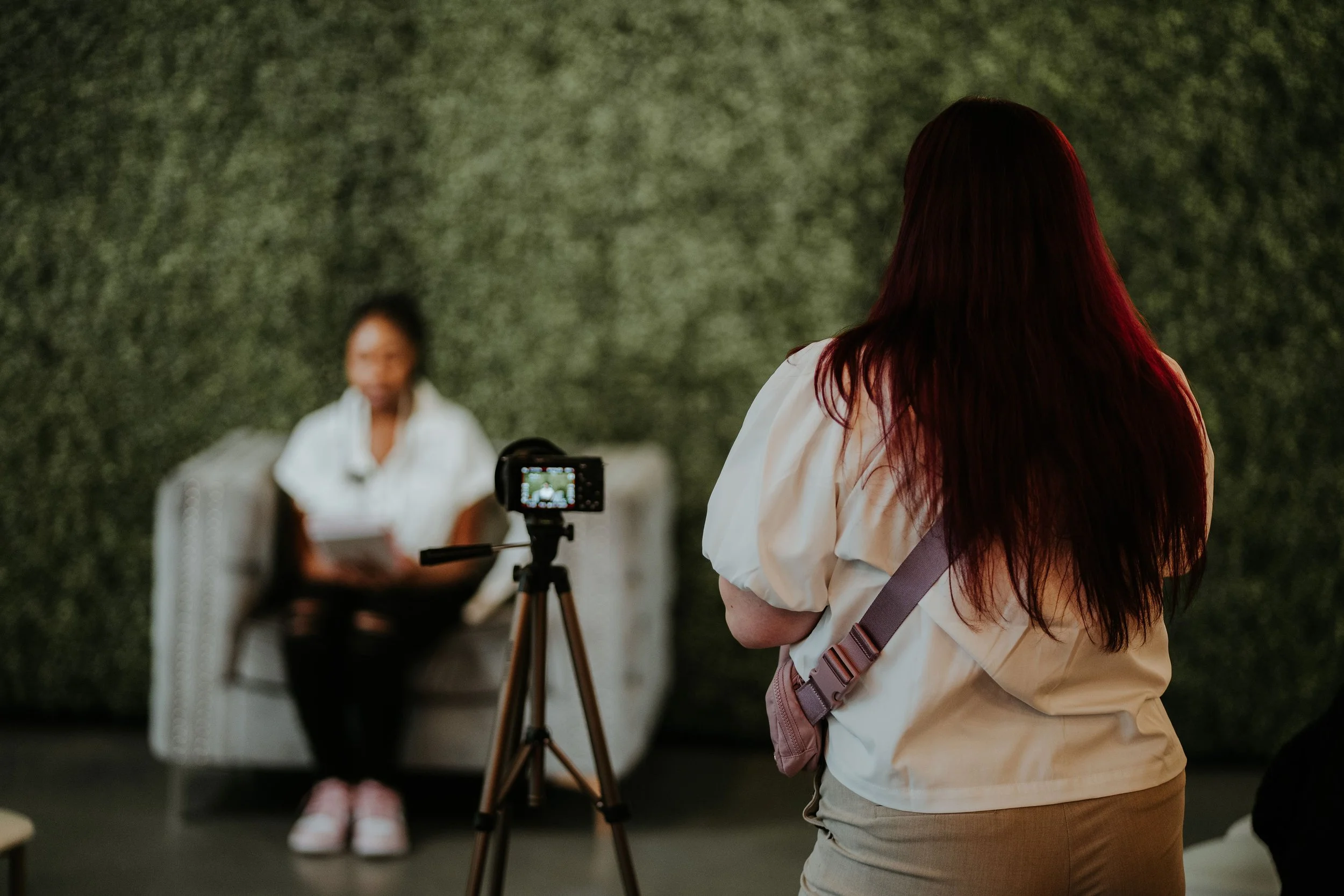 Videographer recording an interview using a camera mounted on a tripod.