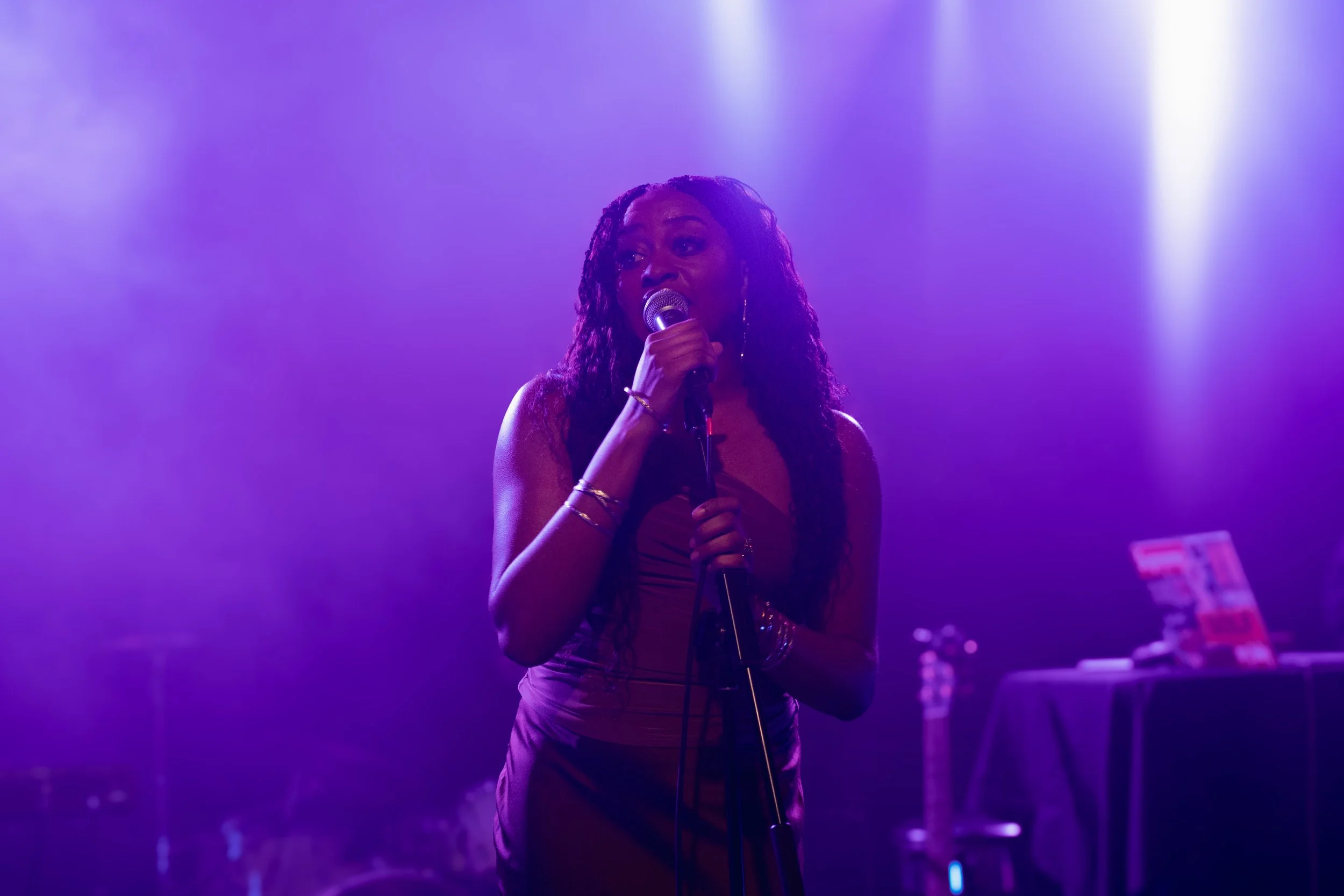Stage performance photograph of a singer under dramatic purple lighting, captured during a live music event.