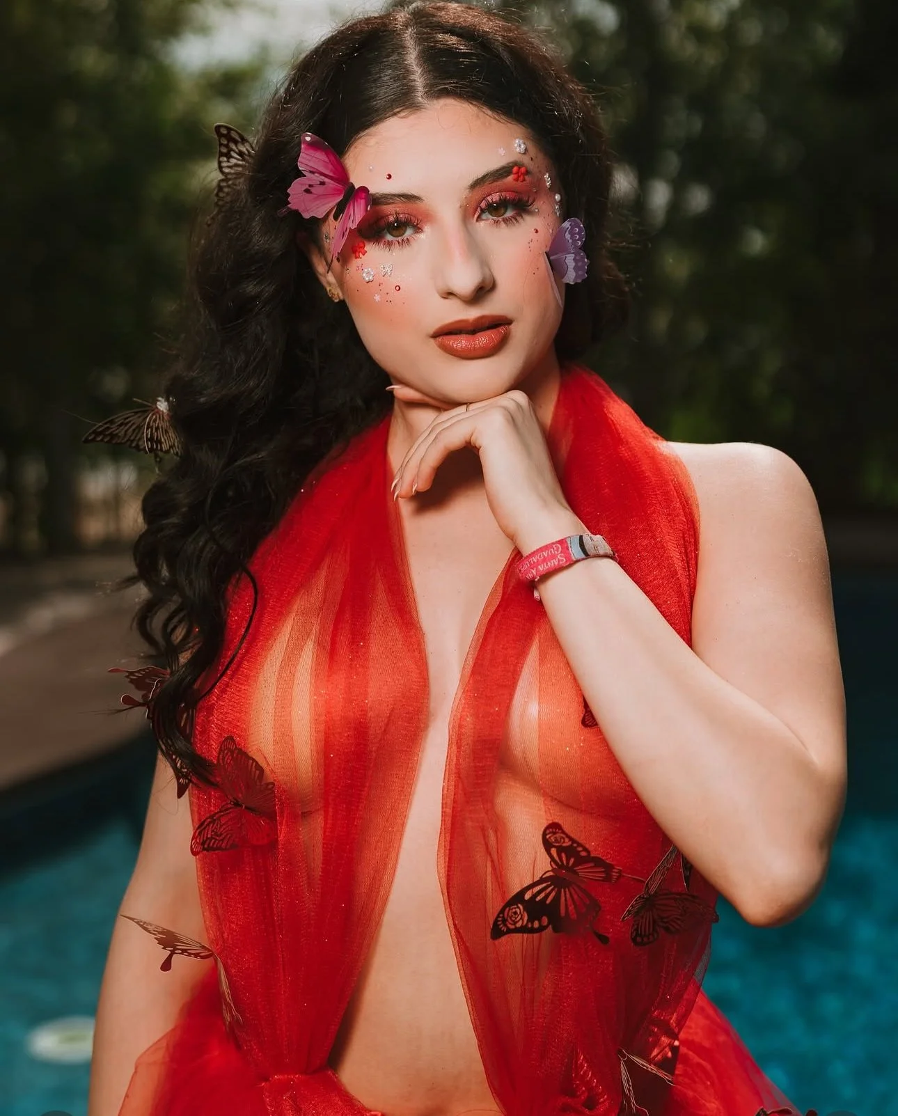 Fashion portrait of a model wearing a sheer red dress with butterfly details and bold makeup.