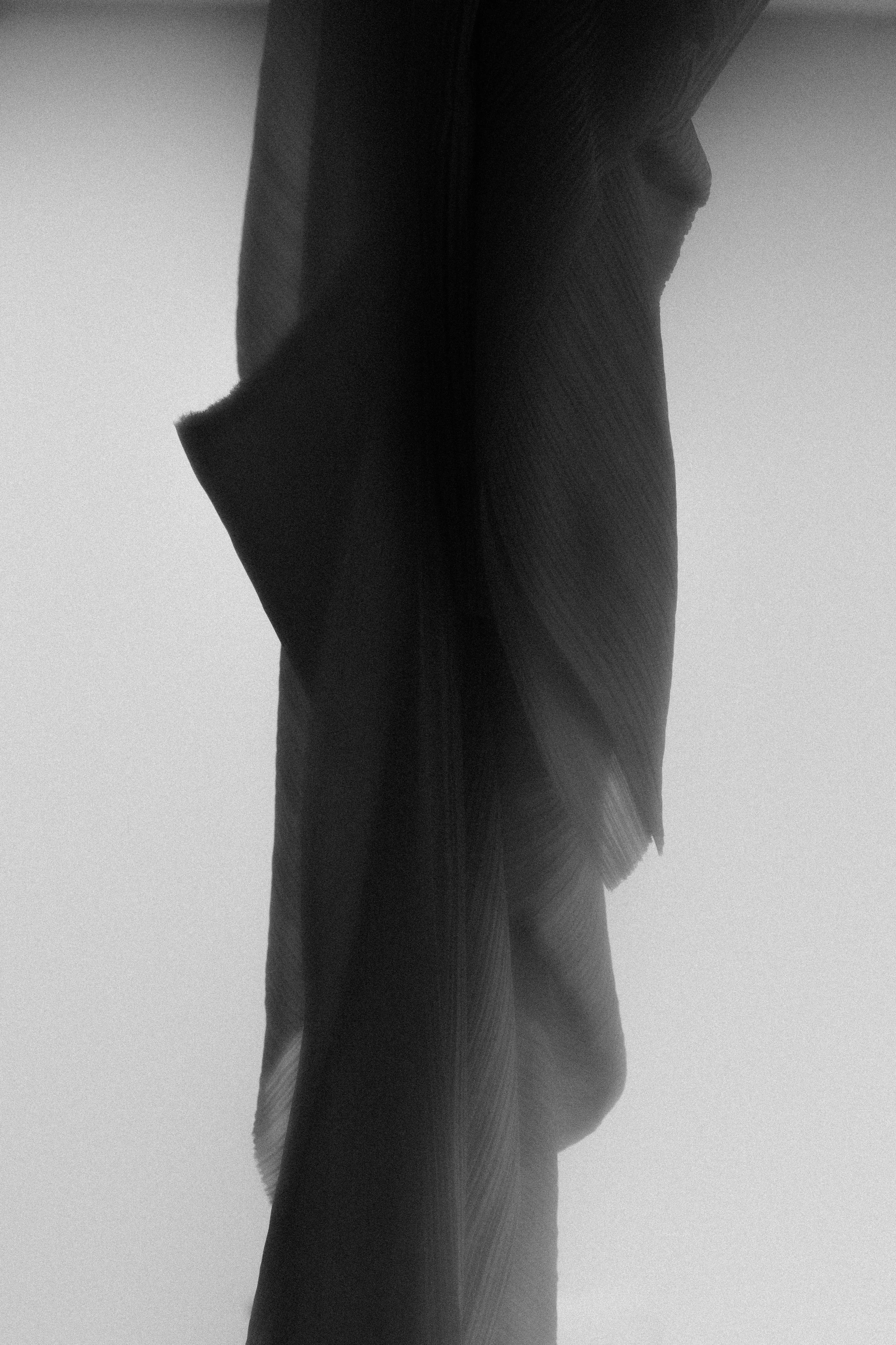OMER ASIM, Close-up of textured fabric or paper with folds and shadows, mostly in black and gray tones.