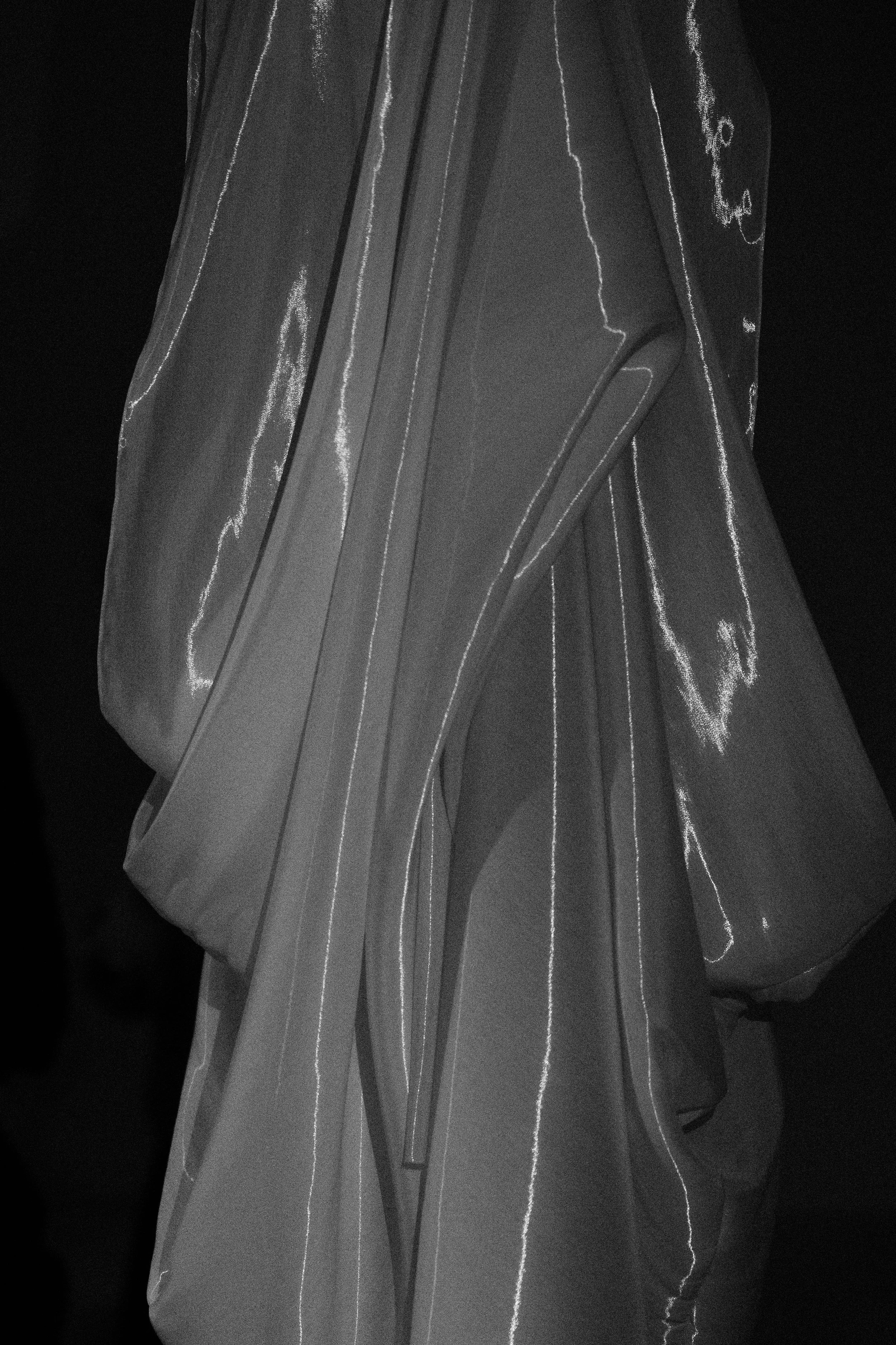 OMER ASIM Close-up of a person wearing a coat with reflective edges, captured in black and white.
