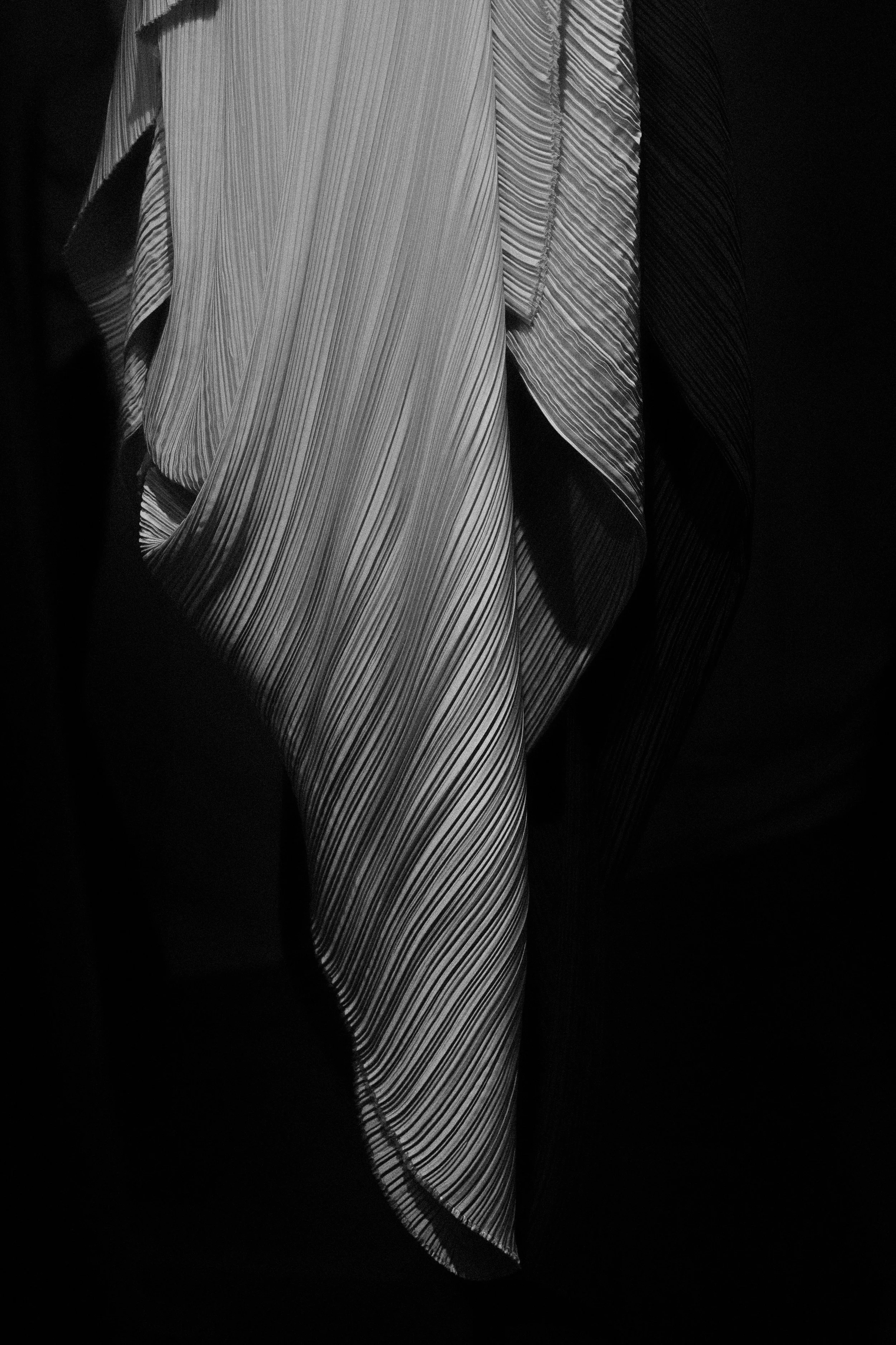 OMER ASIM, Close-up of draped, pleated fabric with vertical and diagonal lines in black and white.