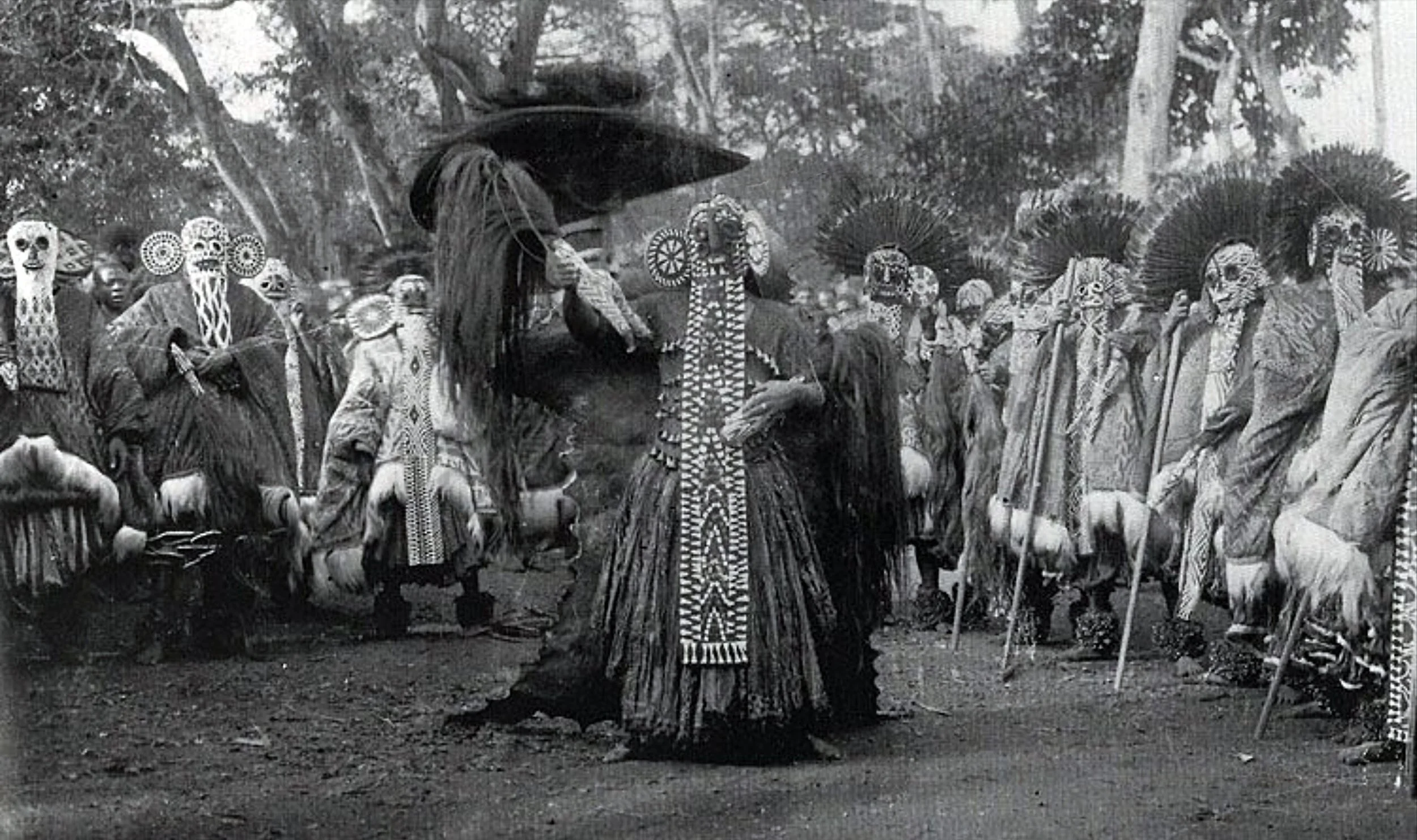 Traditional African ceremony with people wearing masks and costumes in an outdoor setting.
