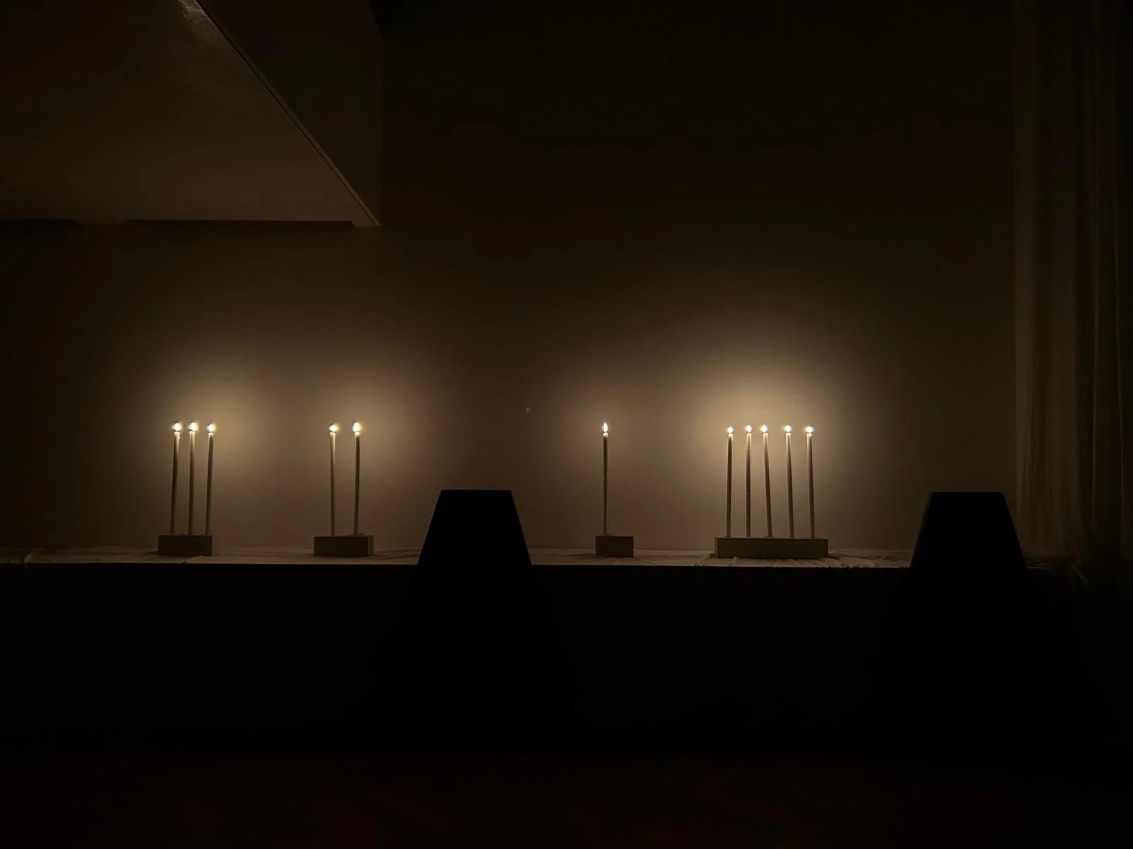 Two sets of lit birthday candles on a table in a dark room, with dim light creating shadows on the wall.