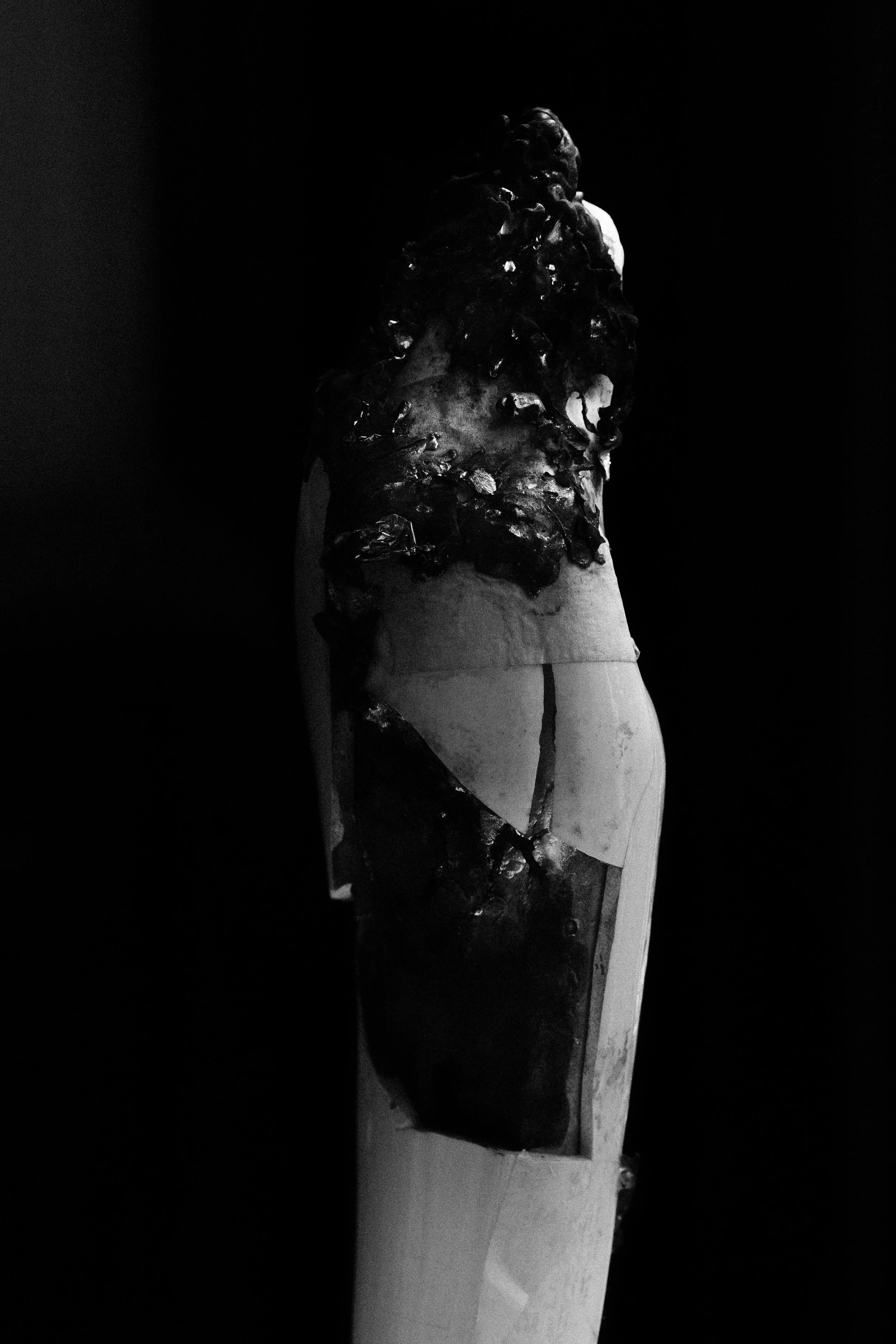 OMER ASIM black and white photograph of a modern sculpture depicting a figure with a textured, abstract upper body and smooth lower body, set against a dark background.