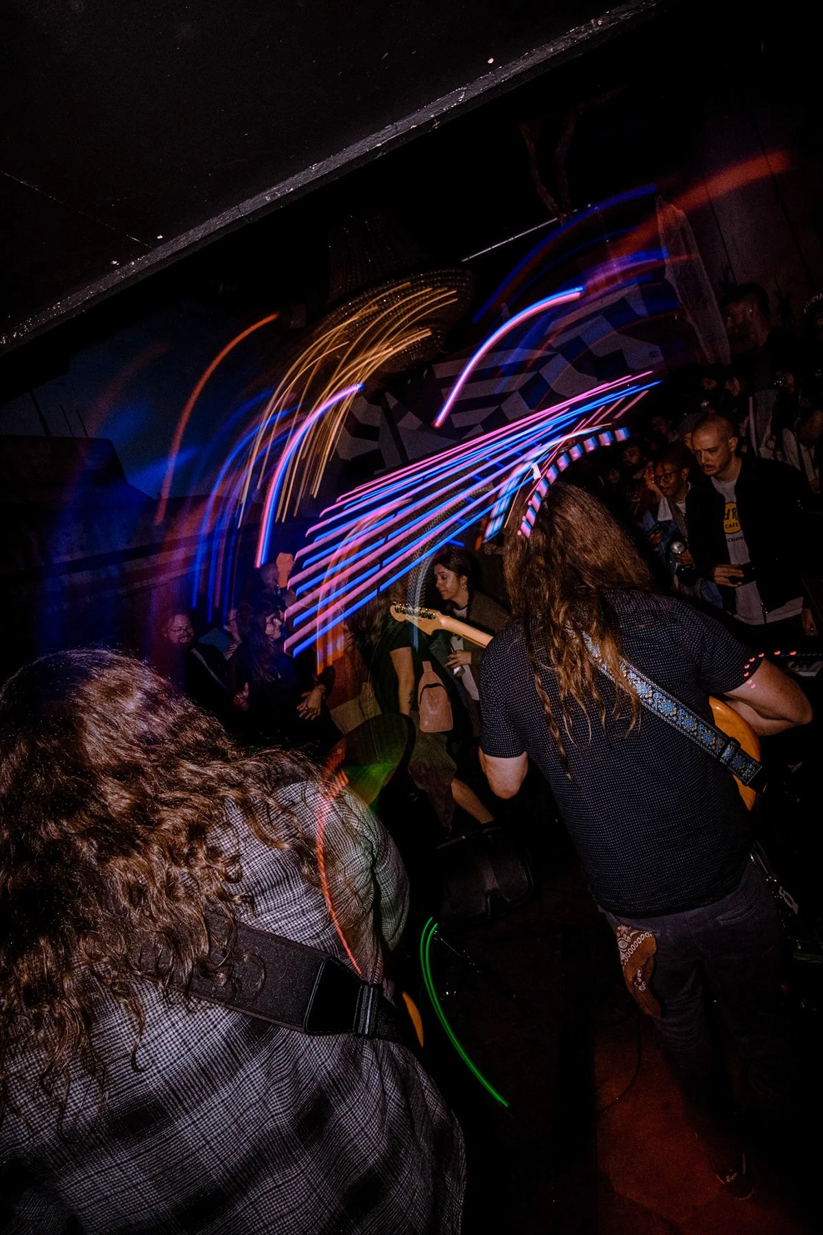 A lively crowd at a concert or nightclub with colorful light trails creating dynamic movement.