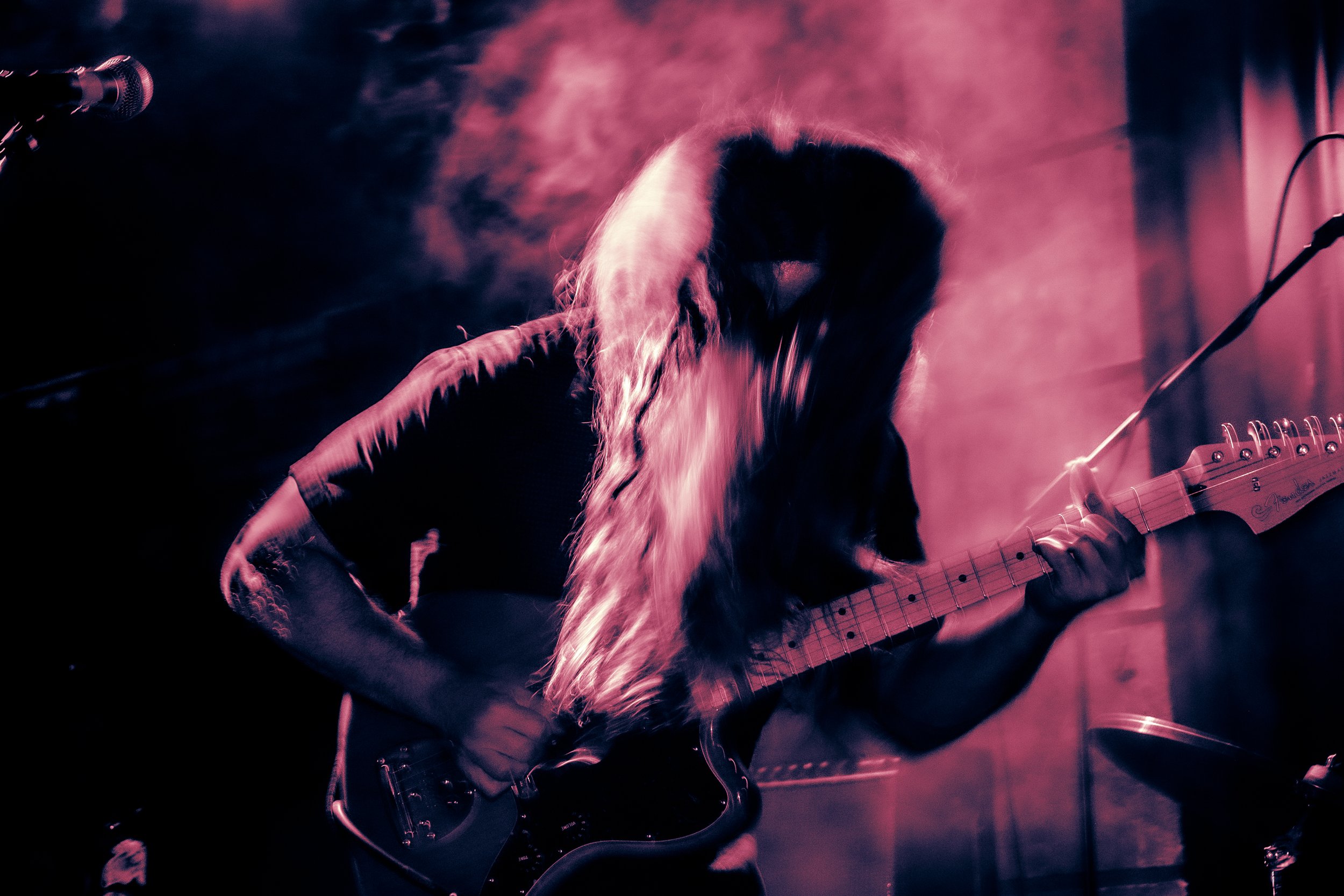 Rock band Liquid Pennies frontman/guitarist Chas BInns playing electric guitar on stage with pink and purple lighting.