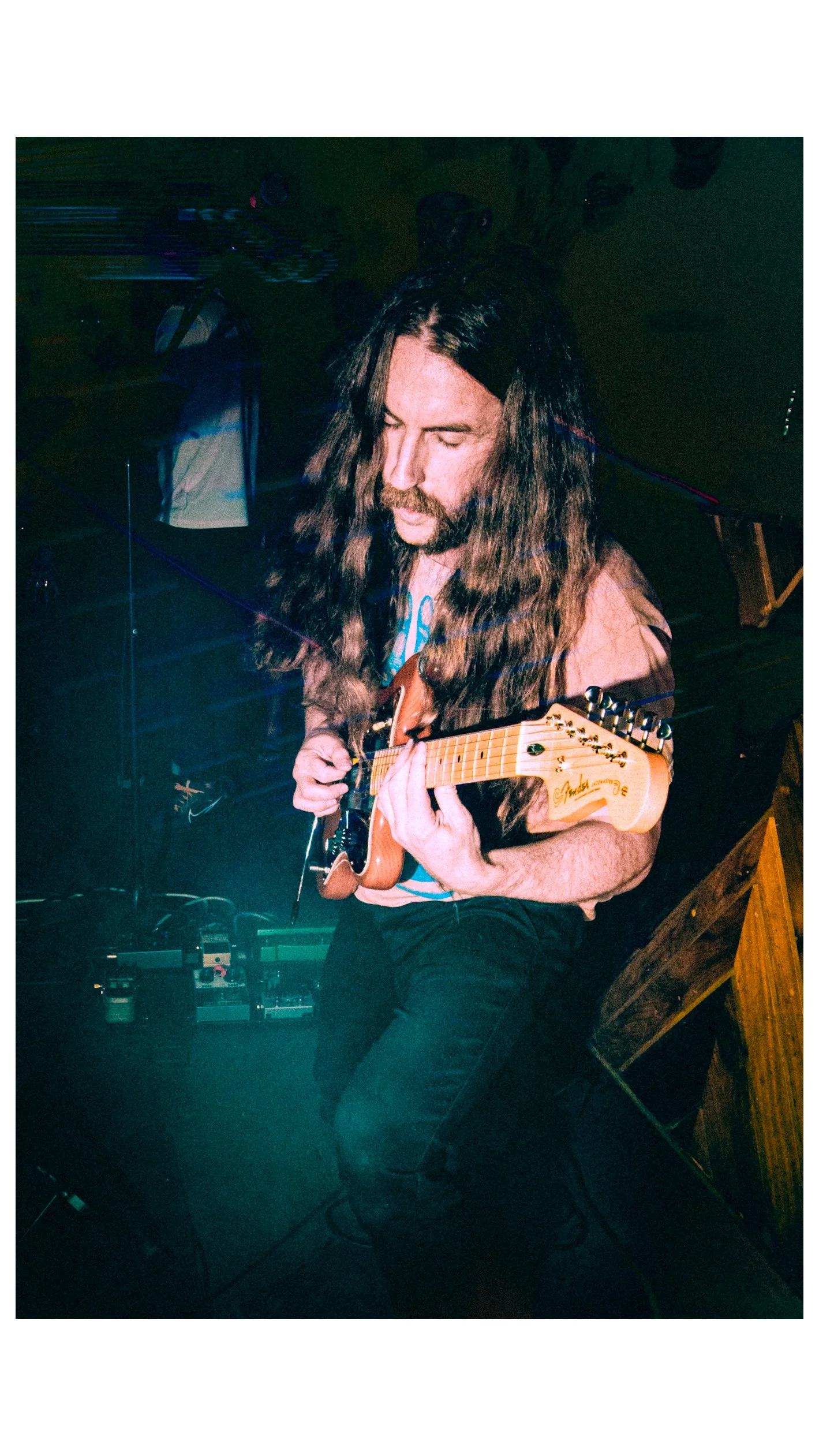 A man with long hair and a beard playing an electric guitar at a music venue. Chas Binns of the band Liquid Pennies playing a Fender Jazzmaster.