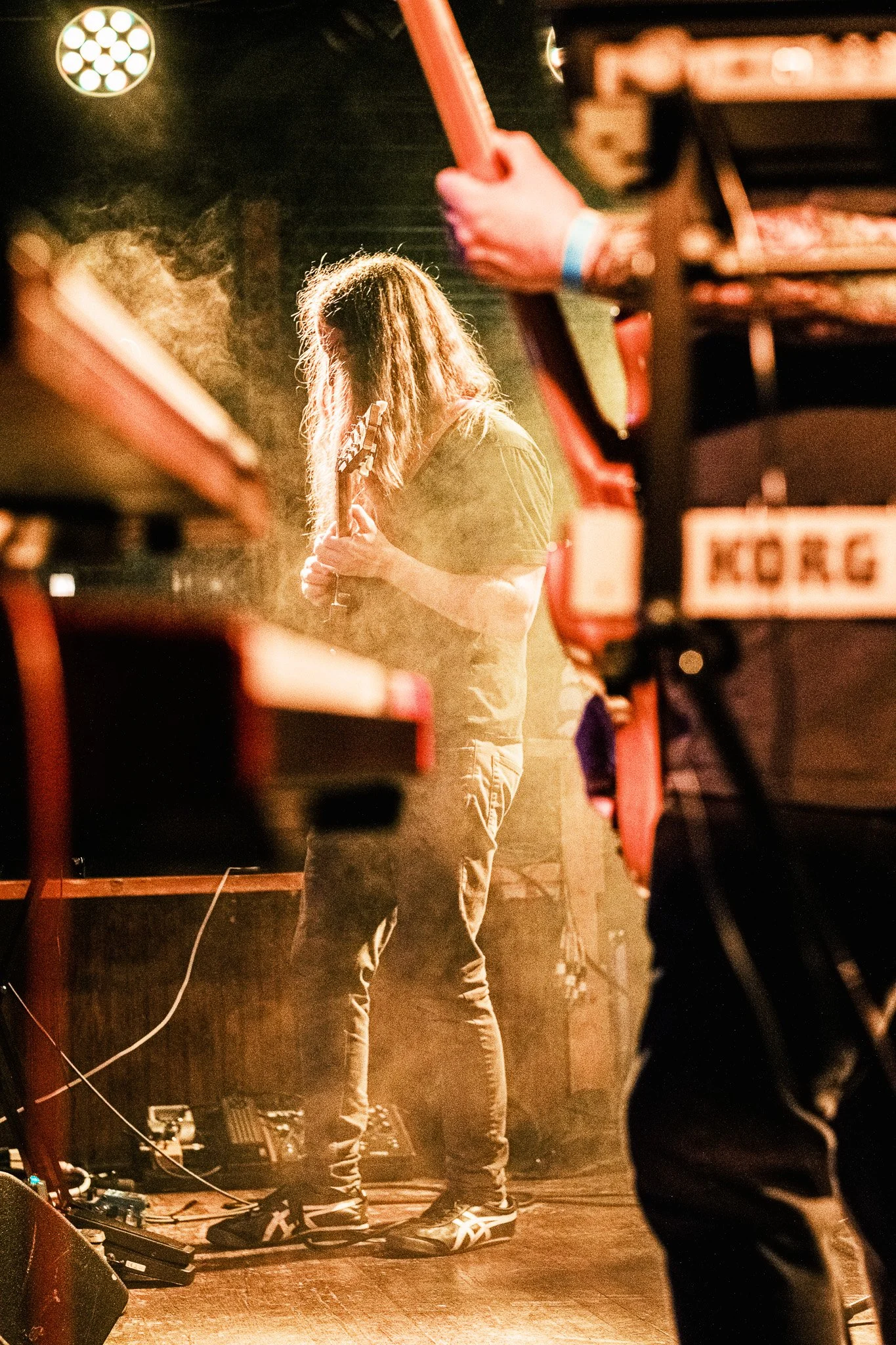 A musician with long, curly hair playing an electric guitar on stage during a performance.