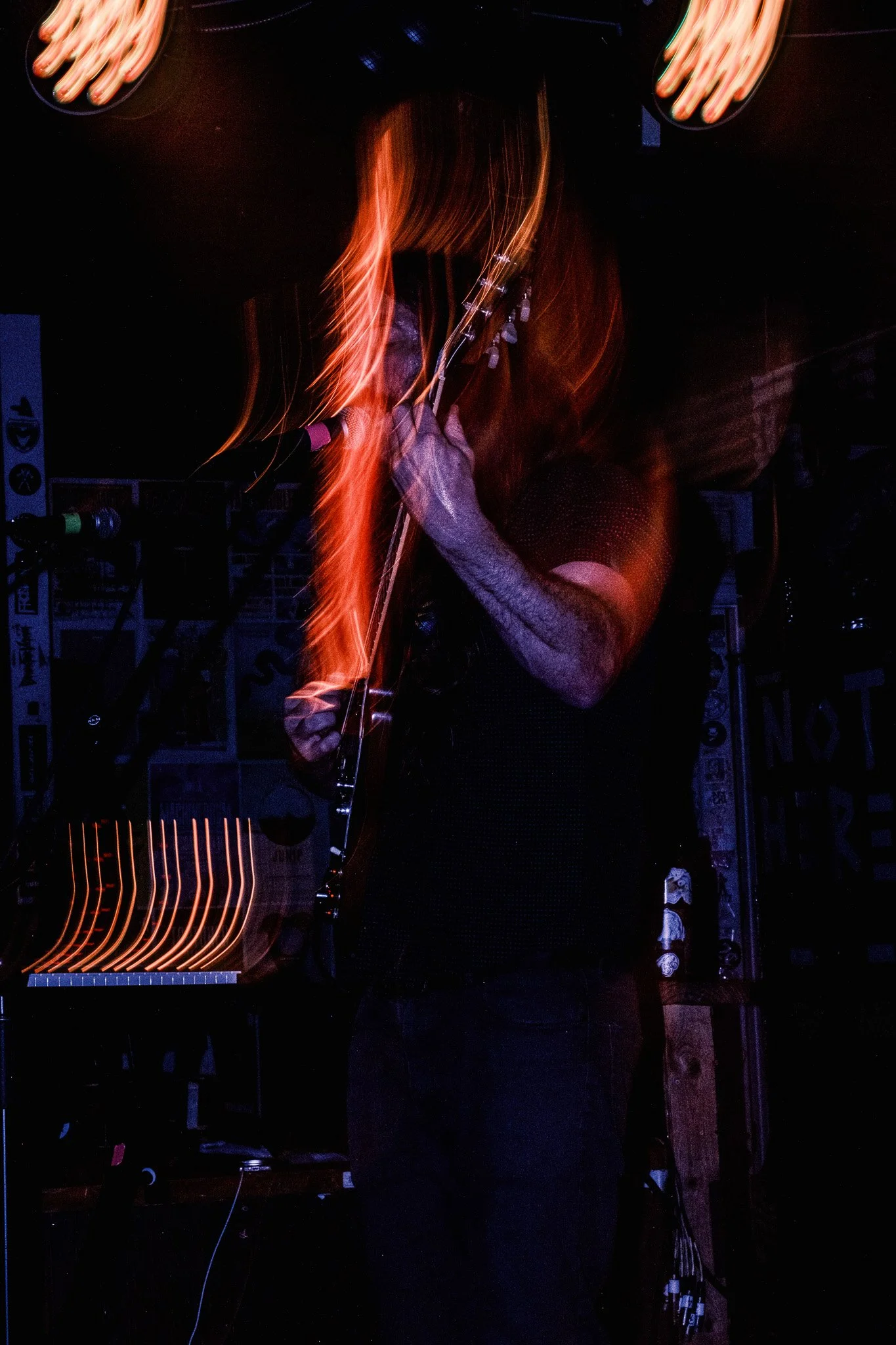 A person playing an electric guitar on stage with vibrant light trails created by motion, in a dimly lit setting, possibly a music venue or bar.