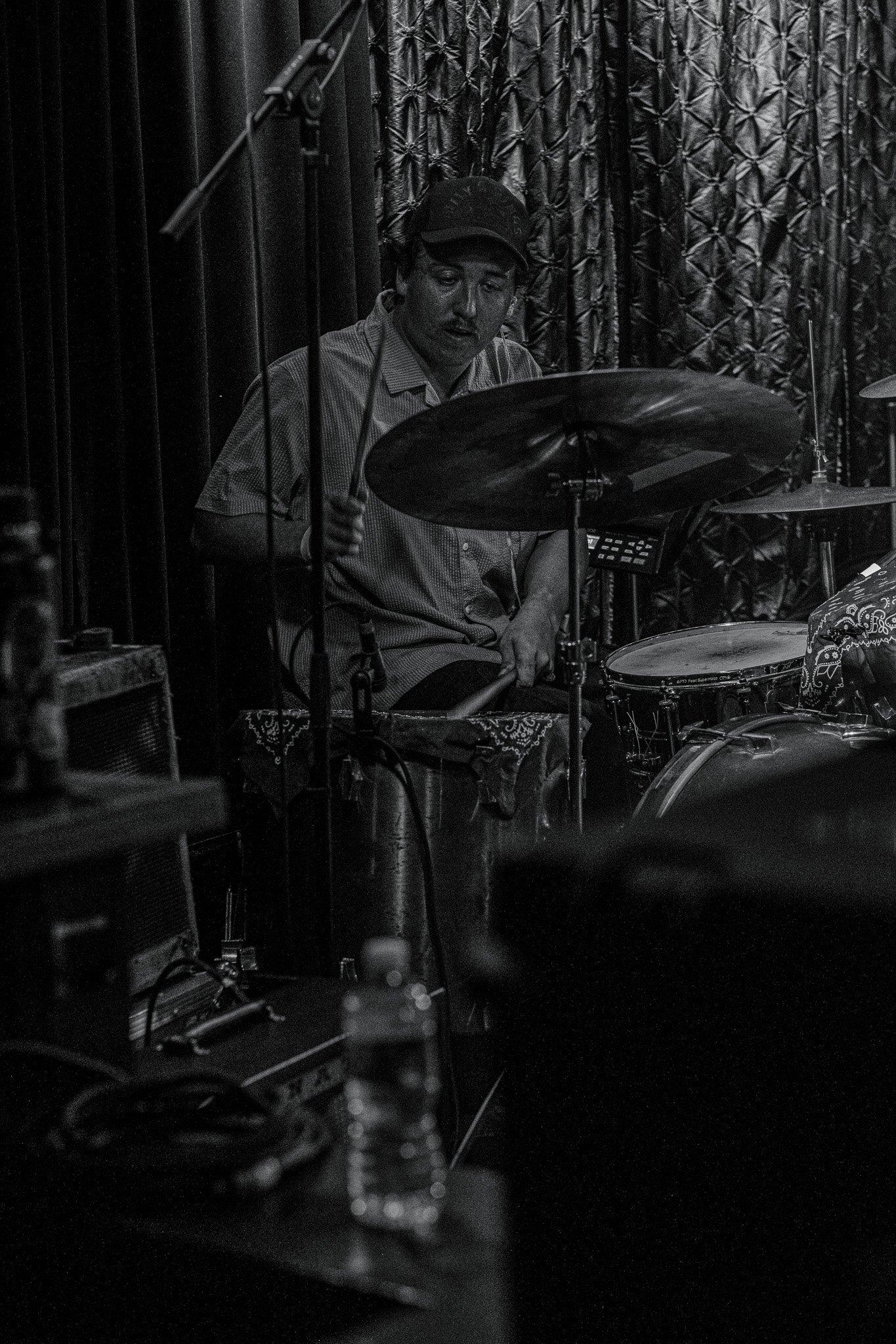 A man playing drums on a stage with dark curtains in the background.
