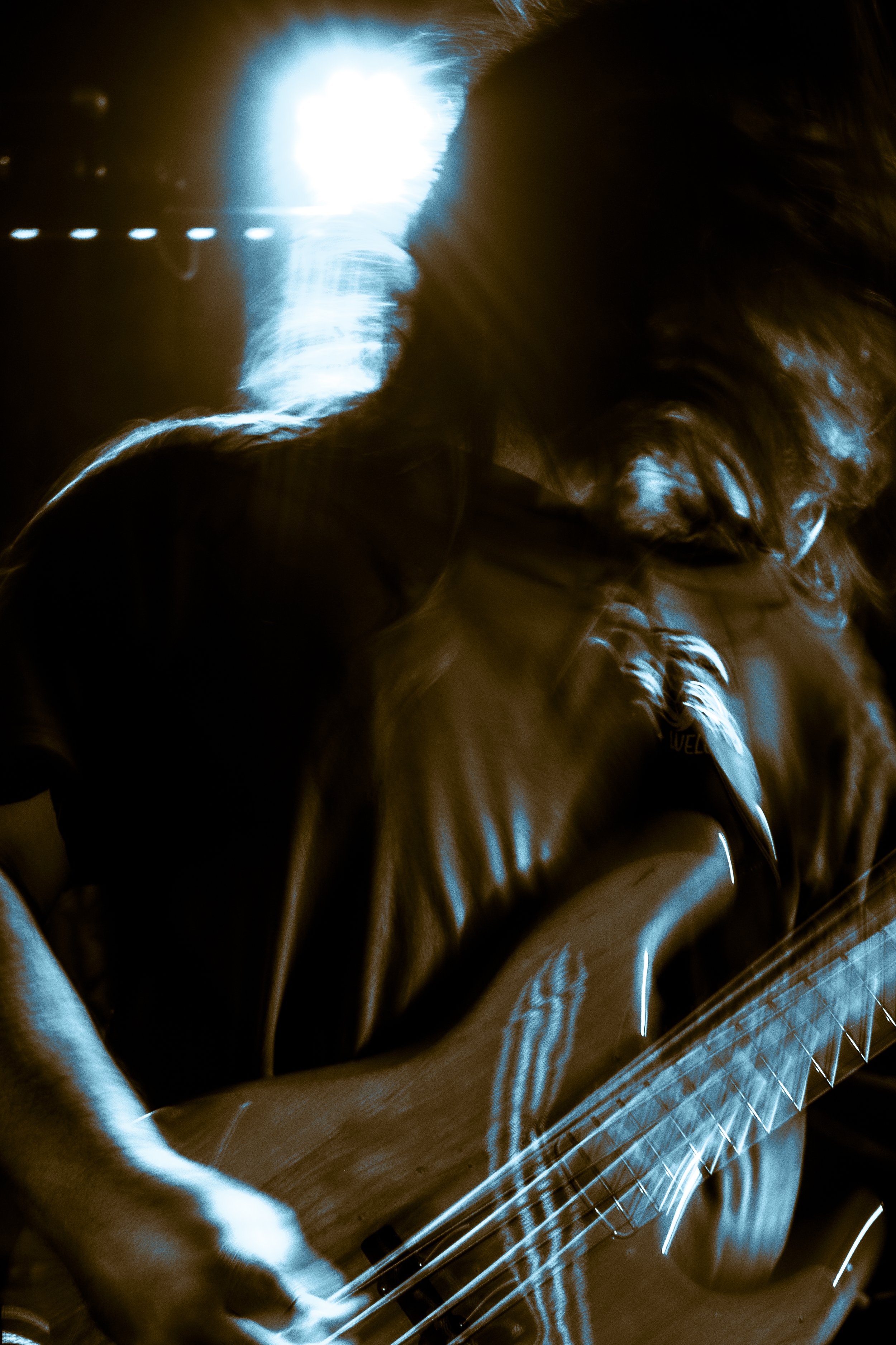 A person with long hair playing an acoustic guitar at night, with bright blue and white light creating motion effects.