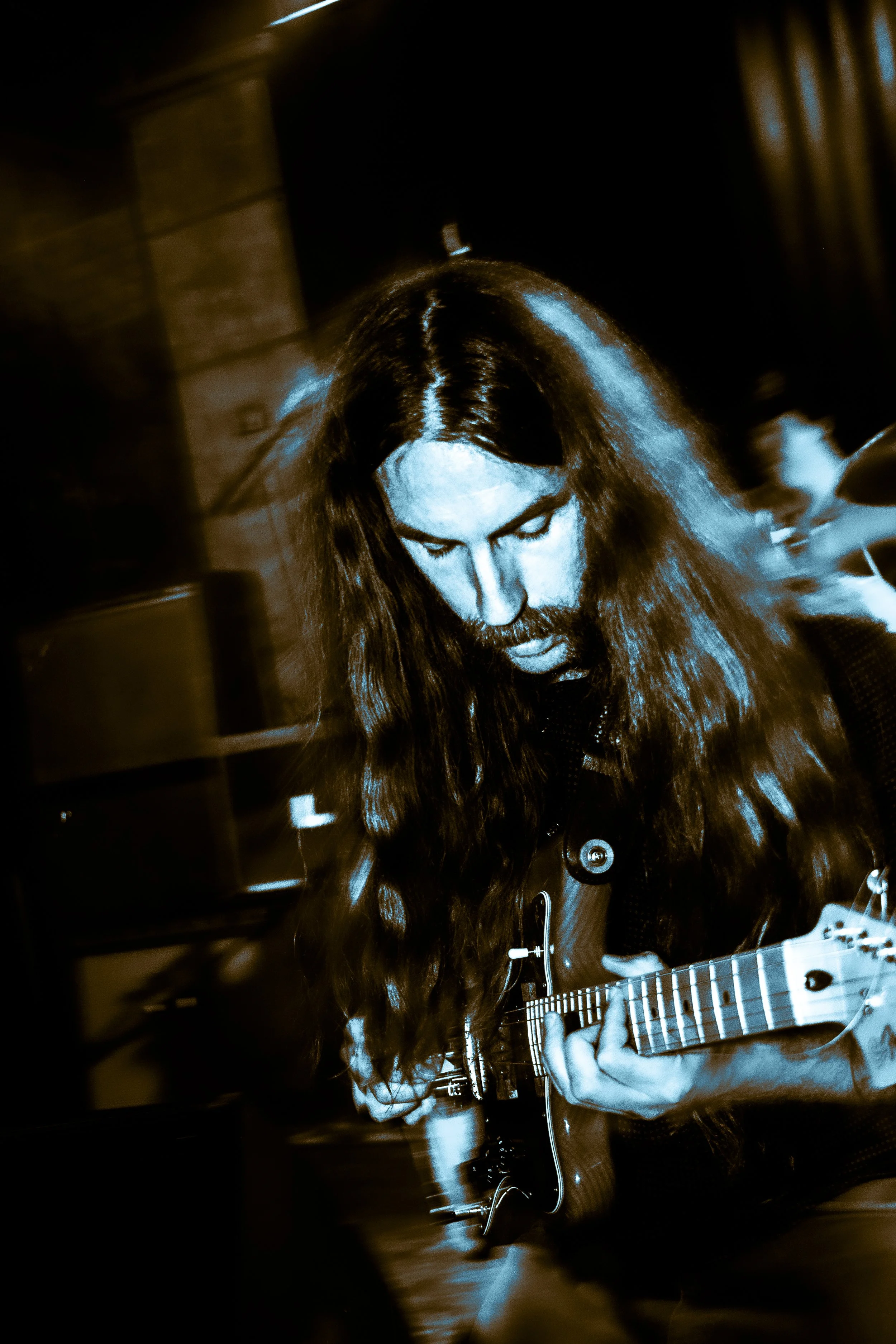 Rock band Liquid Pennies frontman/guitarist Chas BInns is playing an electric guitar, looking down at it, with a blurred background.