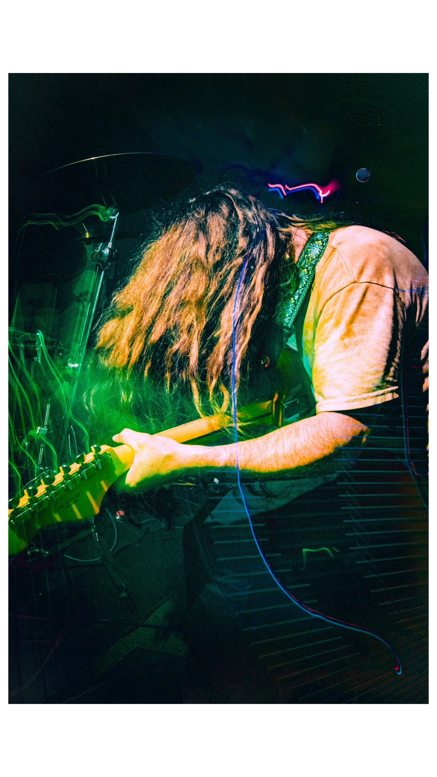 Chas Binns of the rock band LIquid Pennies an electric guitar on stage under colorful lights, showing kinetic live performance energy.