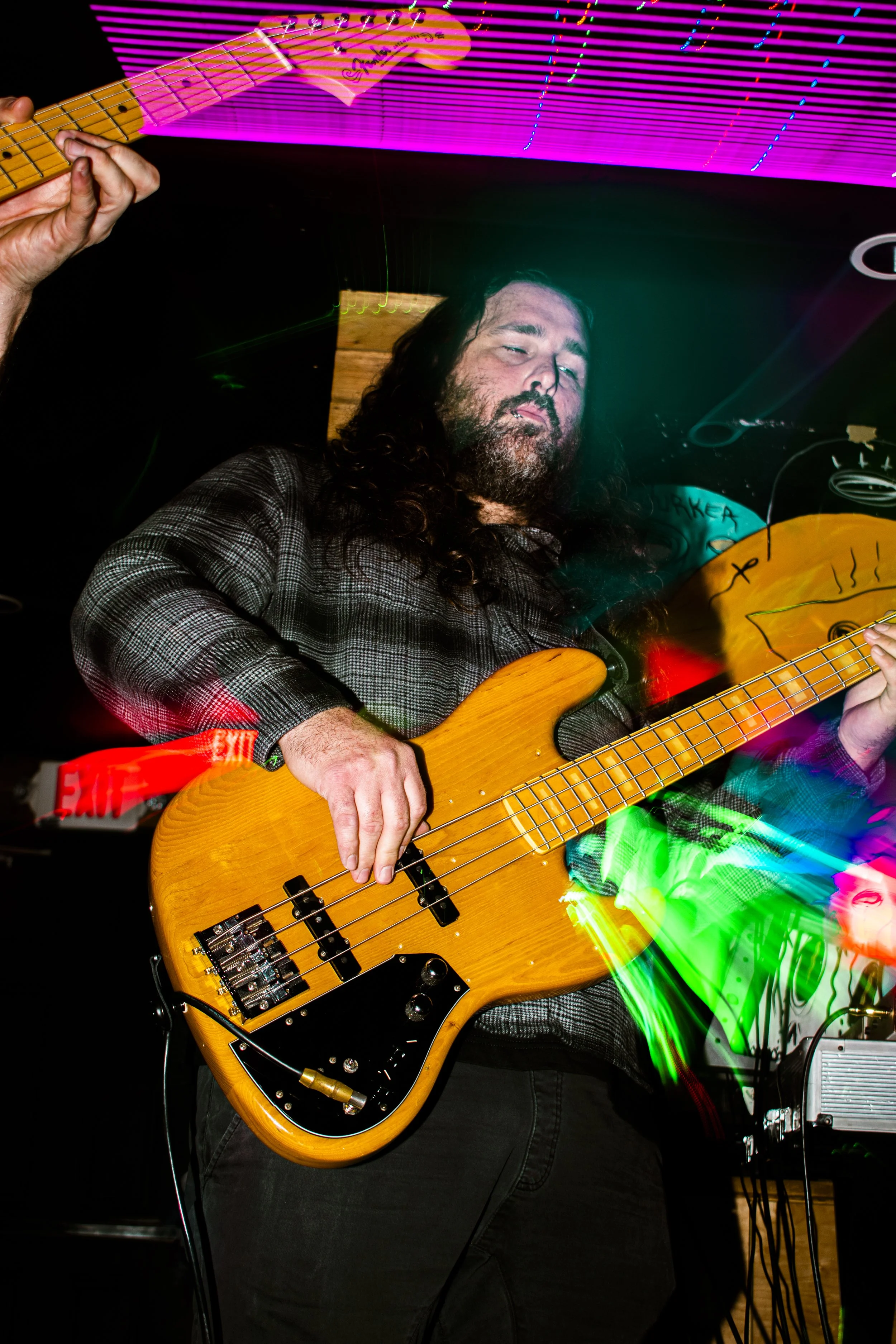 Tysonious Mink of the psych rock band Liquid Pennies playing a yellow electric bass guitar, surrounded by colorful light streaks during a live music performance.