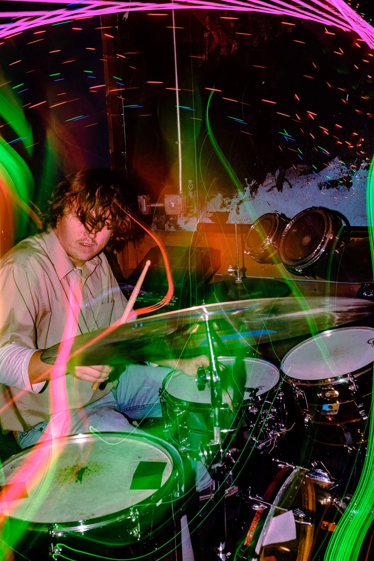 A man playing drums under colorful, swirling light trails in a dark setting.