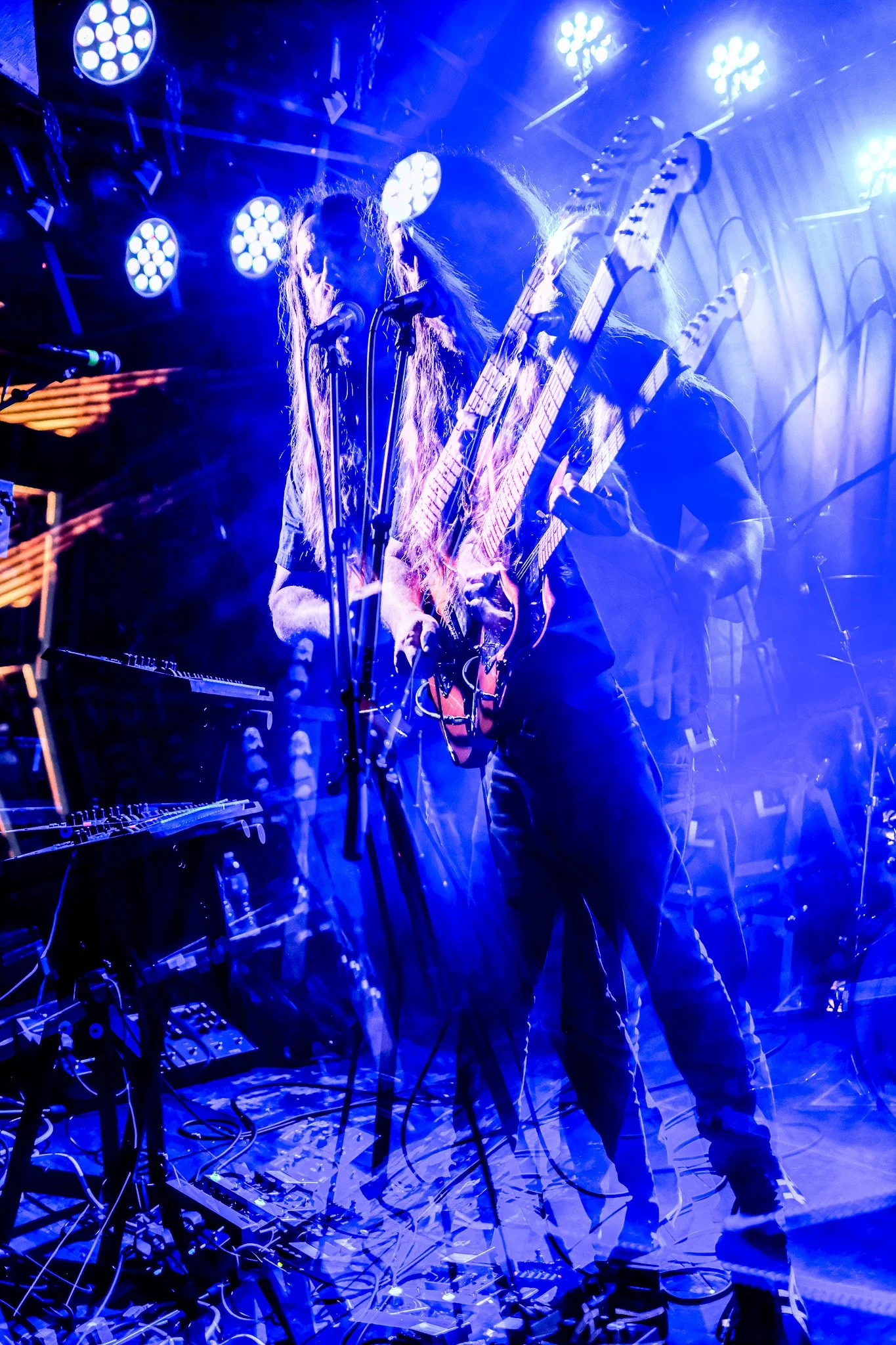 Musicians performing on stage under bright blue and white stage lights with layered effects creating a dynamic, multi-exposure appearance.