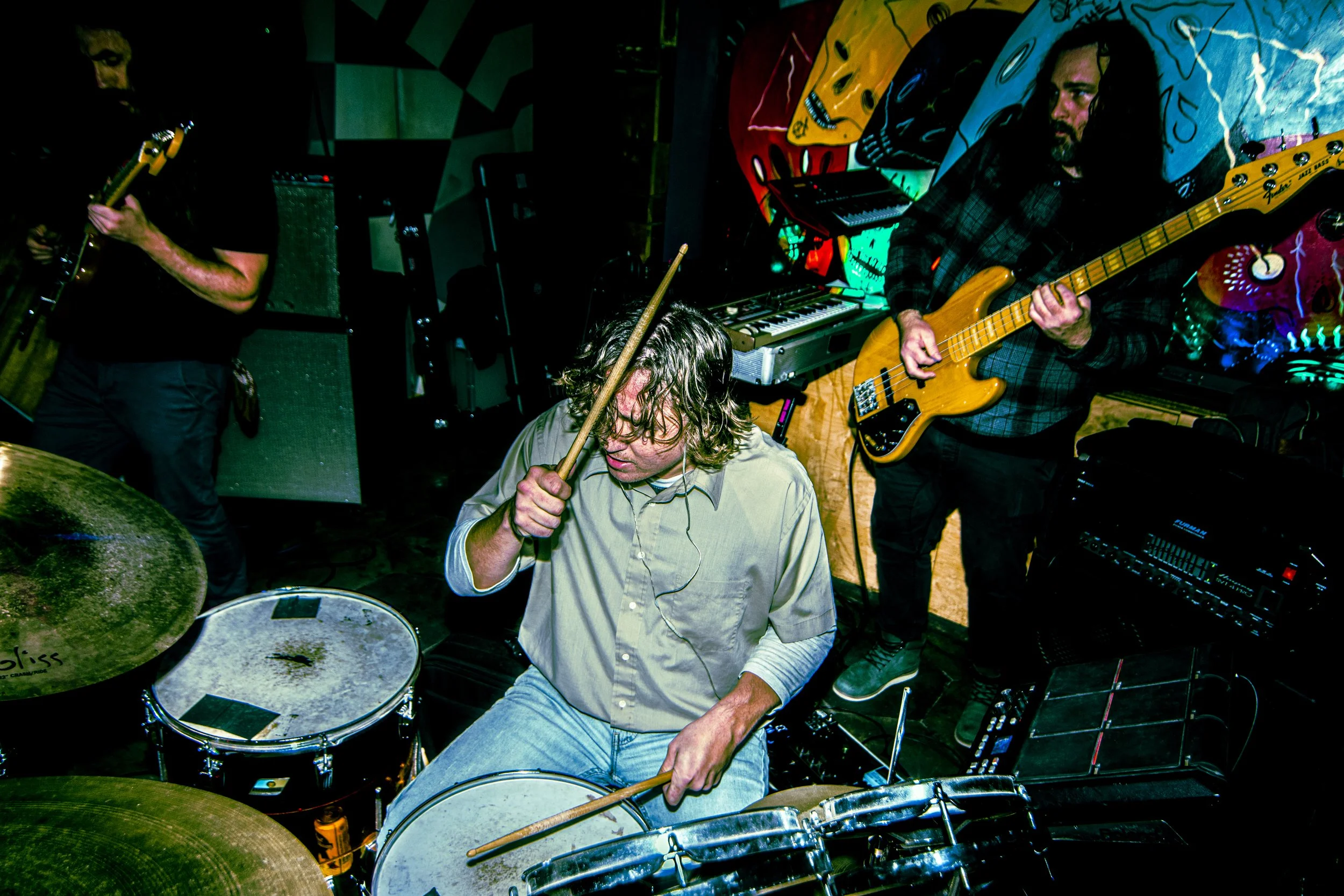 Three musicians performing live, with one on drums, another on bass guitar, and the third playing electric guitar.