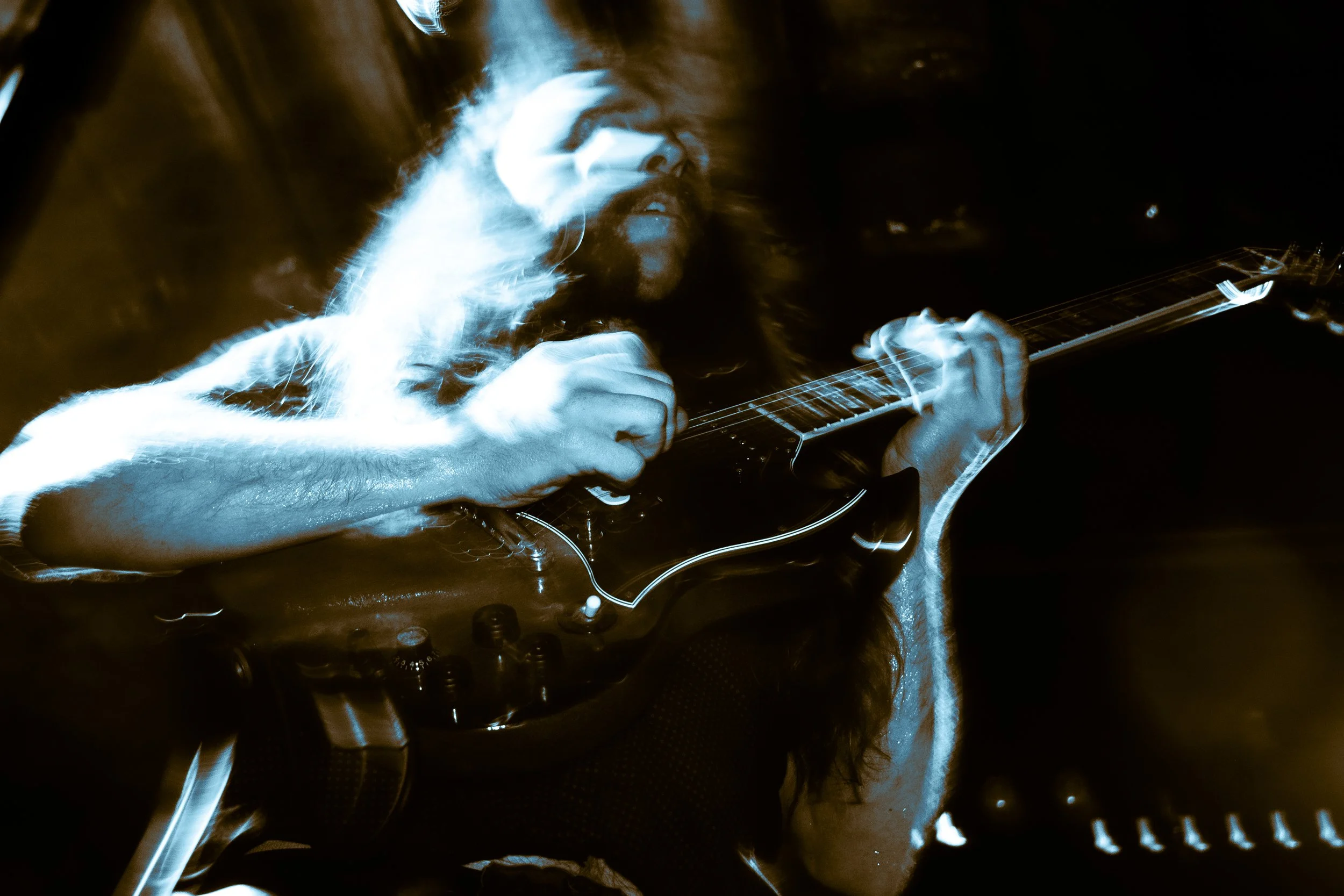 A musician playing an electric guitar during a live performance, illuminated with blue lighting and motion blur effects.