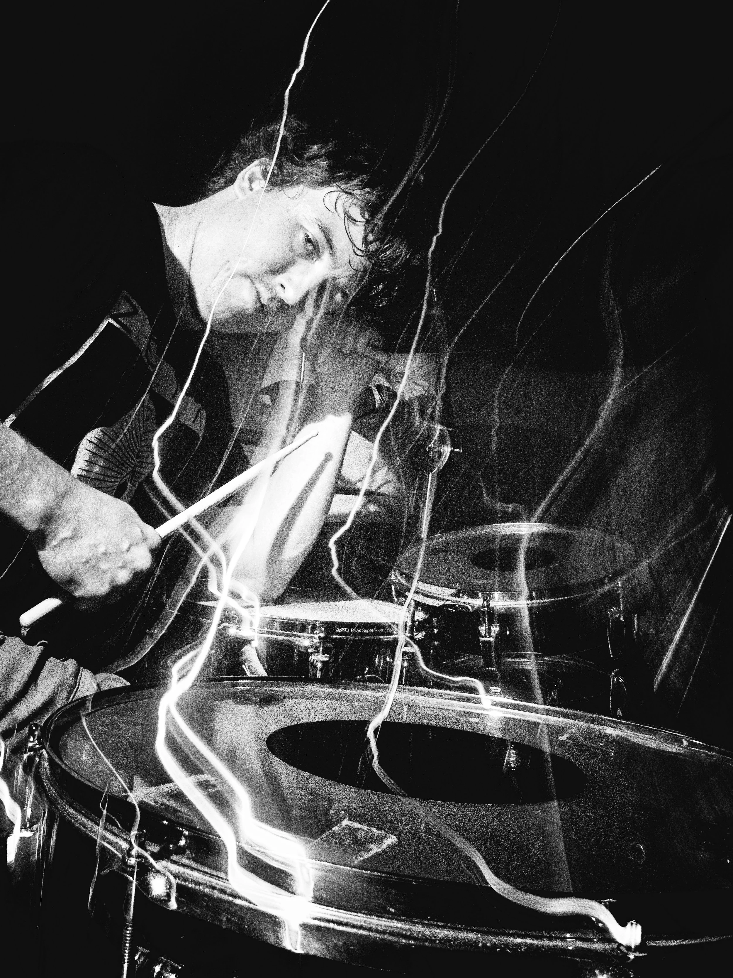 Black and white photo of a drummer playing drums with motion blur and light streaks.