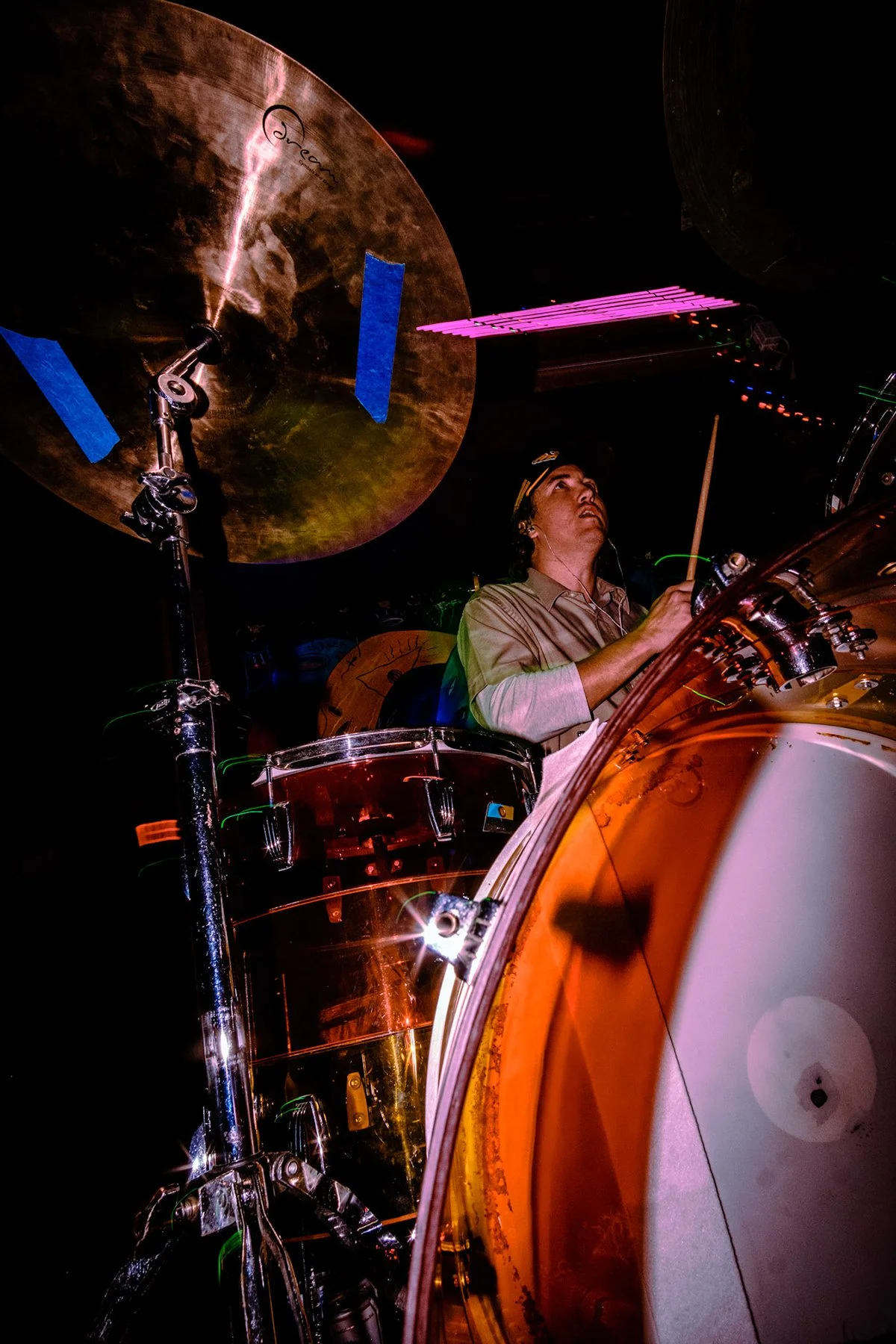 Liquid Pennies drummer Pierson Whicker playing a drum set on stage under colorful lighting, with a large cymbal overhead.