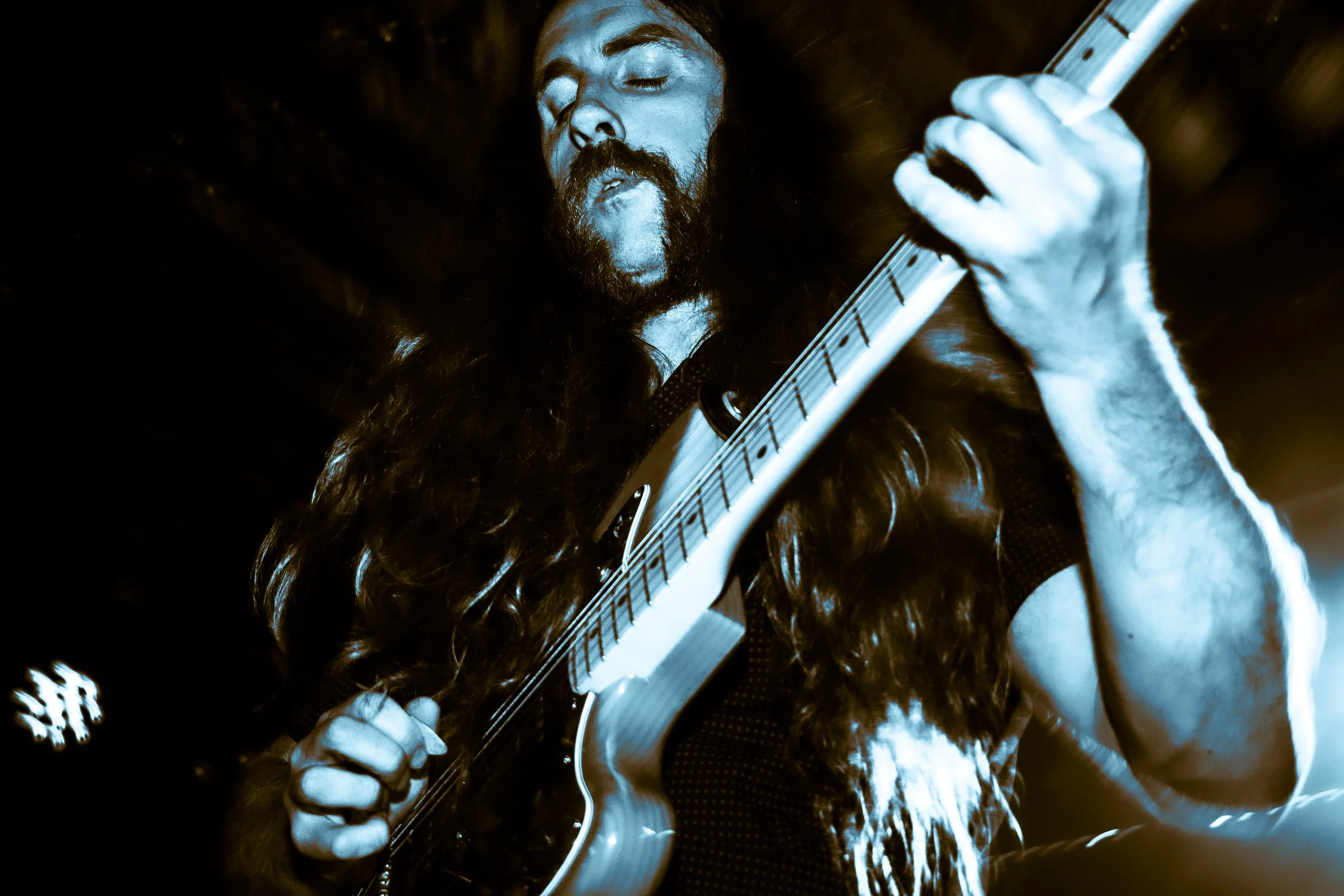 Rock band Liquid Pennies frontman/guitarist Chas BInns playing a Fender Jazzmaster electric guitar with his eyes closed in a dark setting.