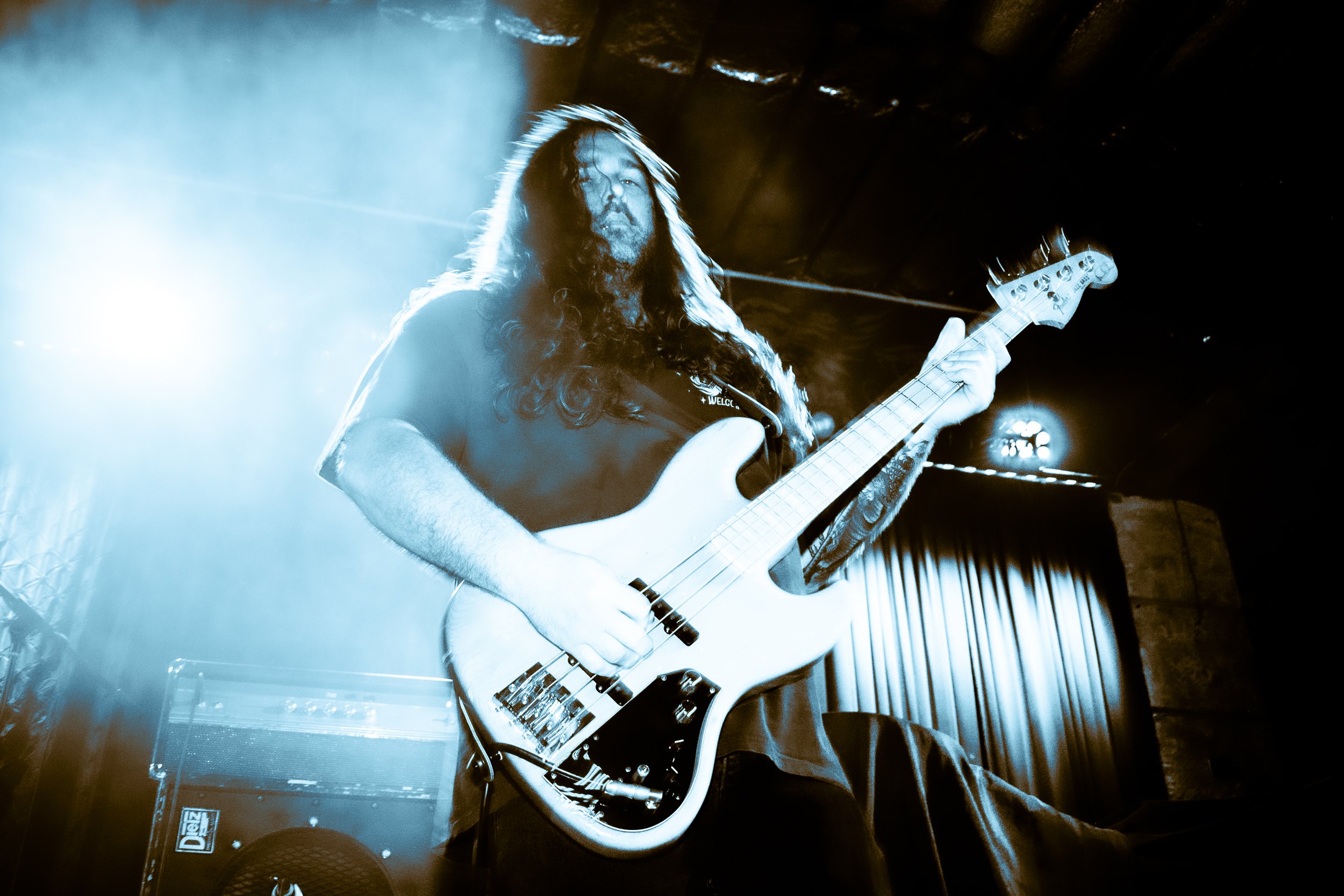 Musician playing electric bass guitar on stage with dramatic lighting and smoke effects.