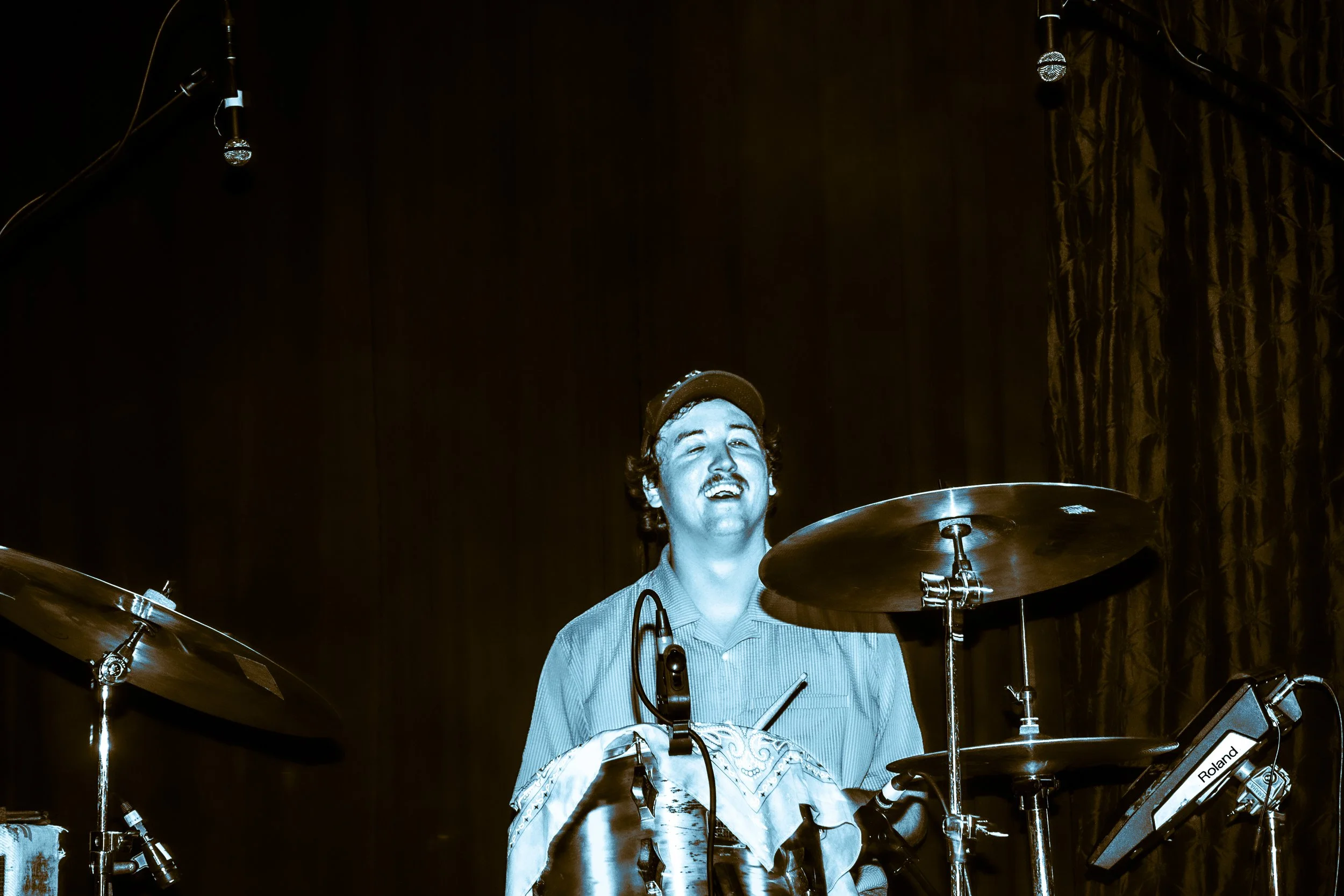 A man smiling while playing drums on a stage.