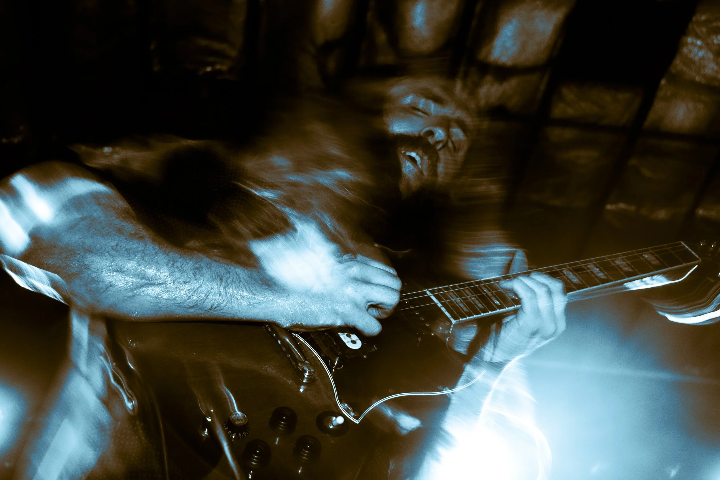 Musician playing electric guitar on stage with intense expression, motion blur, and blue lighting