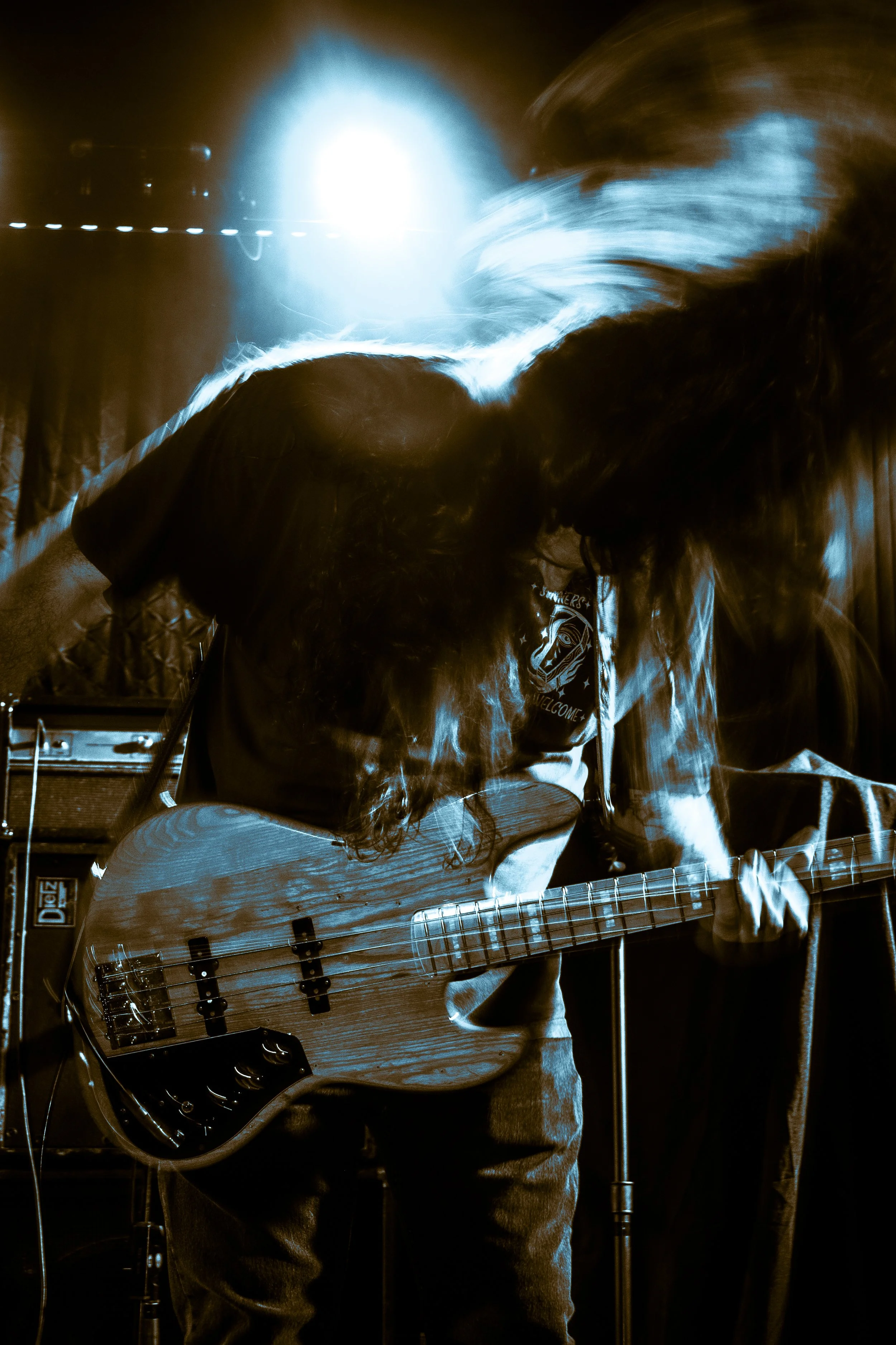 Musician playing an electric bass guitar on stage with blue lighting and motion effects.