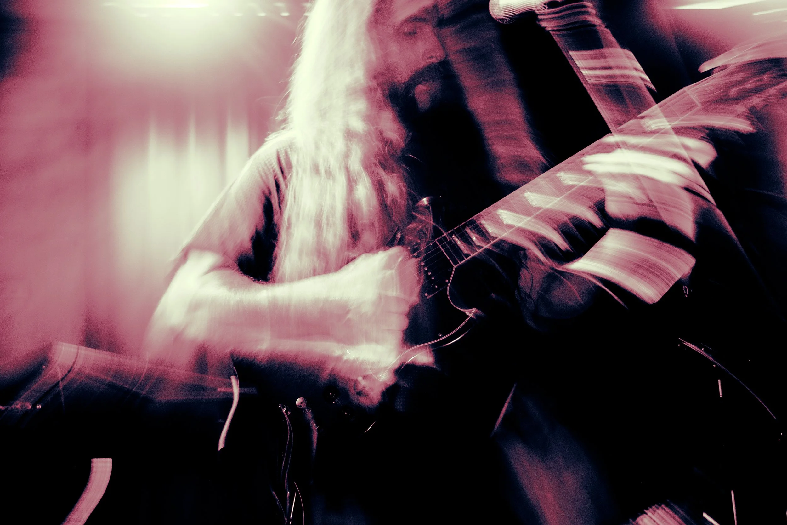 Rock band Liquid Pennies frontman/guitarist Chas BInns playing an electric guitar, with motion blur and colorful lighting effects.