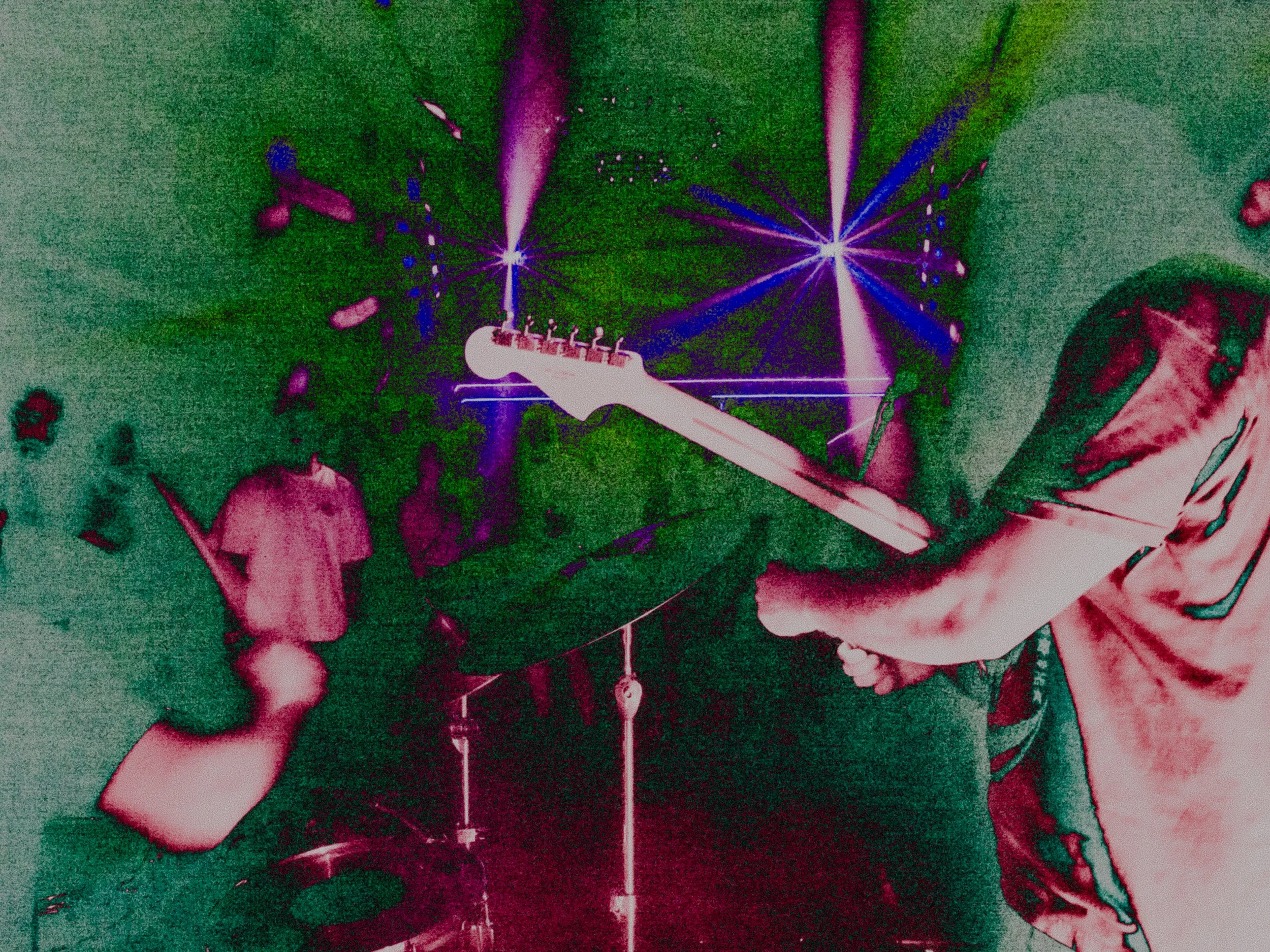 Person playing electric guitar in a dark setting with colorful lights and shadows.